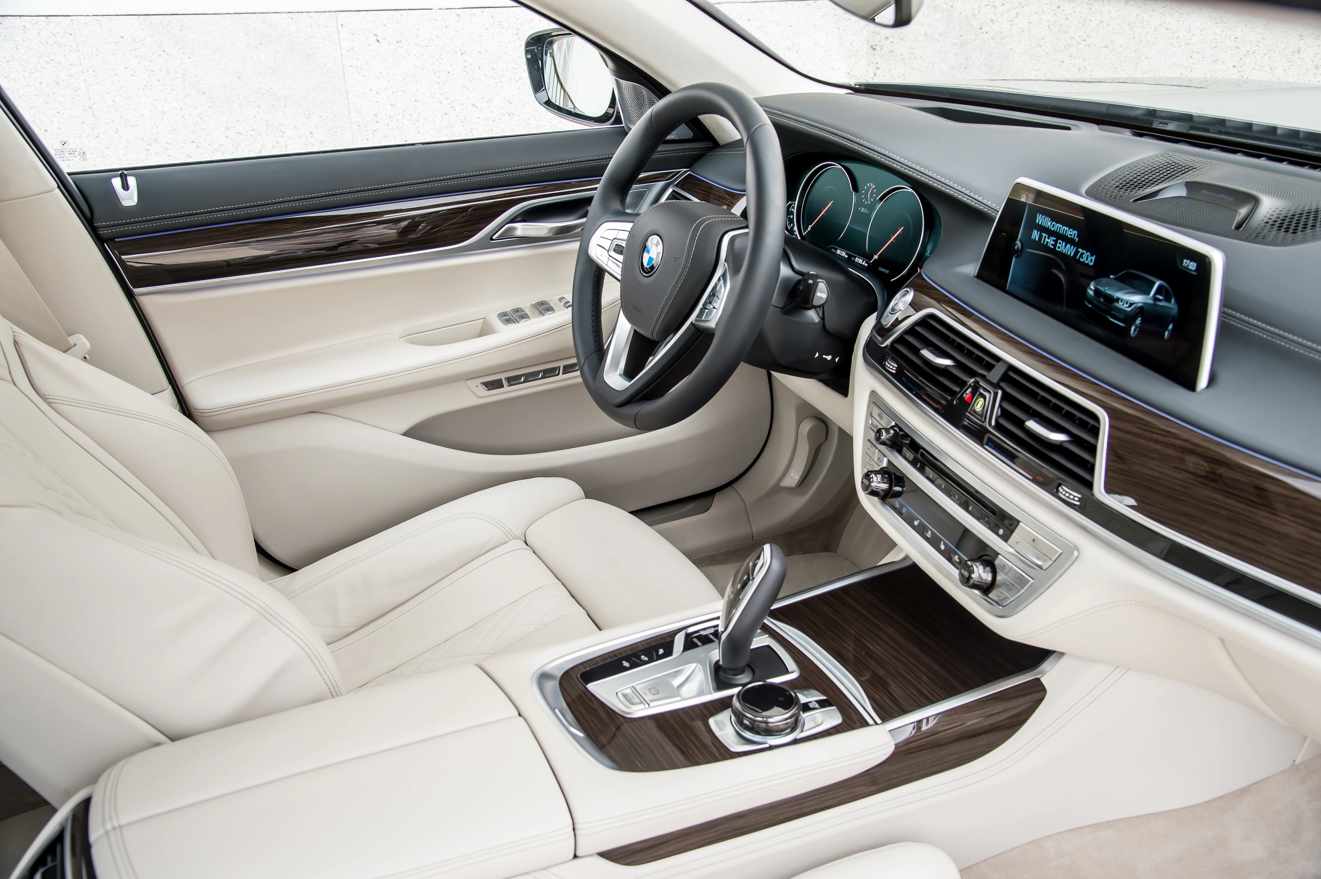 Innenraum eines luxuriösen Autos mit beige Ledersitzen, Holzverkleidung, modernem Lenkrad und Touchscreen-Display auf der Mittelkonsole.