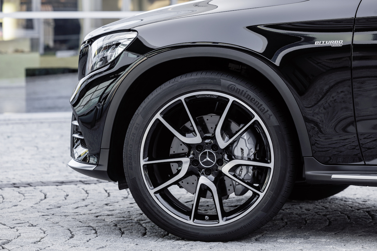 Nahaufnahme eines schwarzen Autos mit silbernen Felgen und einem „BITURBO“ Emblem, das auf einer gepflasterten Straße steht.