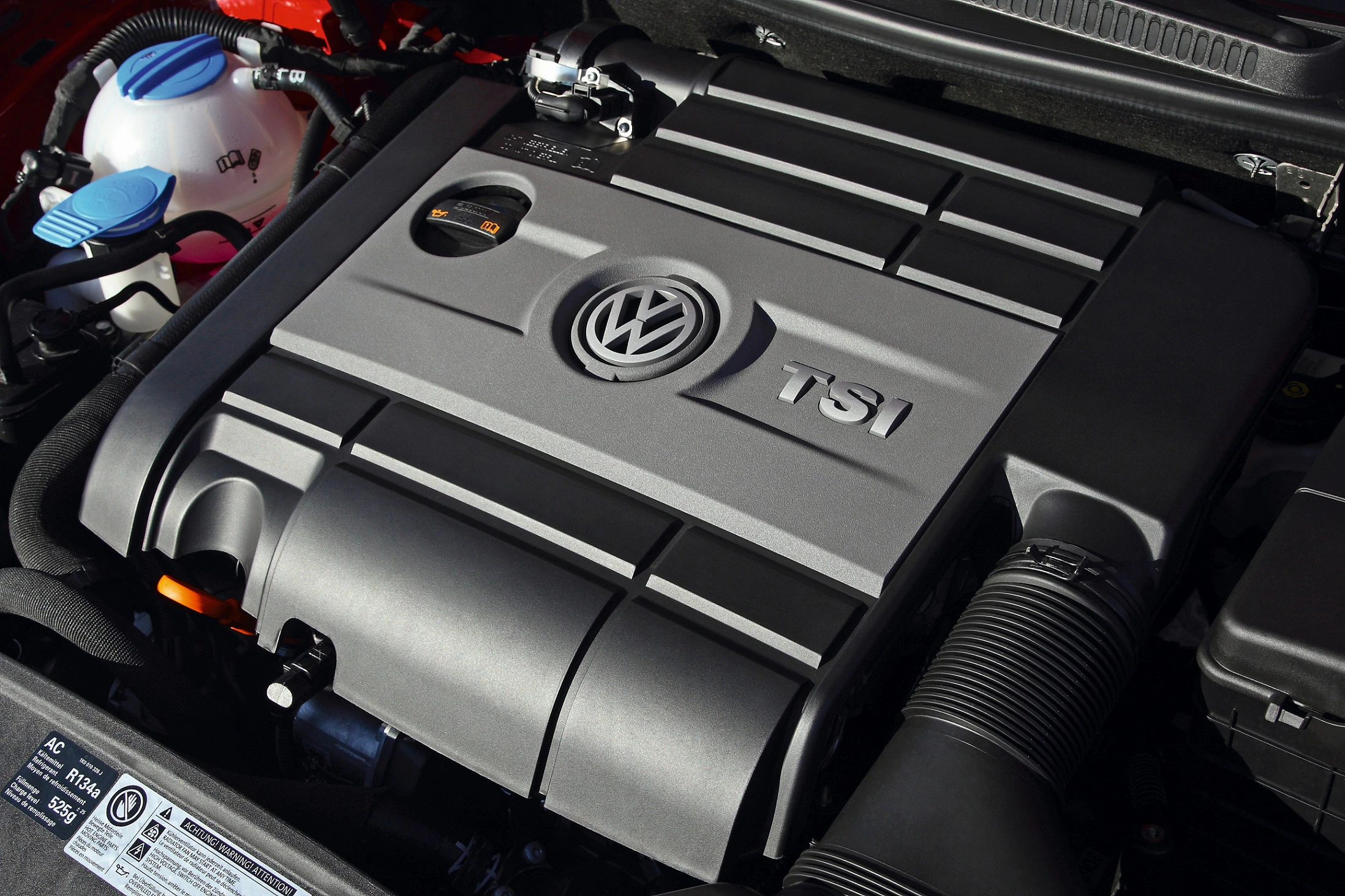 Motor eines Volkswagen-Fahrzeugs mit TSI-Technologie. Sichtbar sind Motorkomponenten und das VW-Logo in einer geordneten Anordnung.