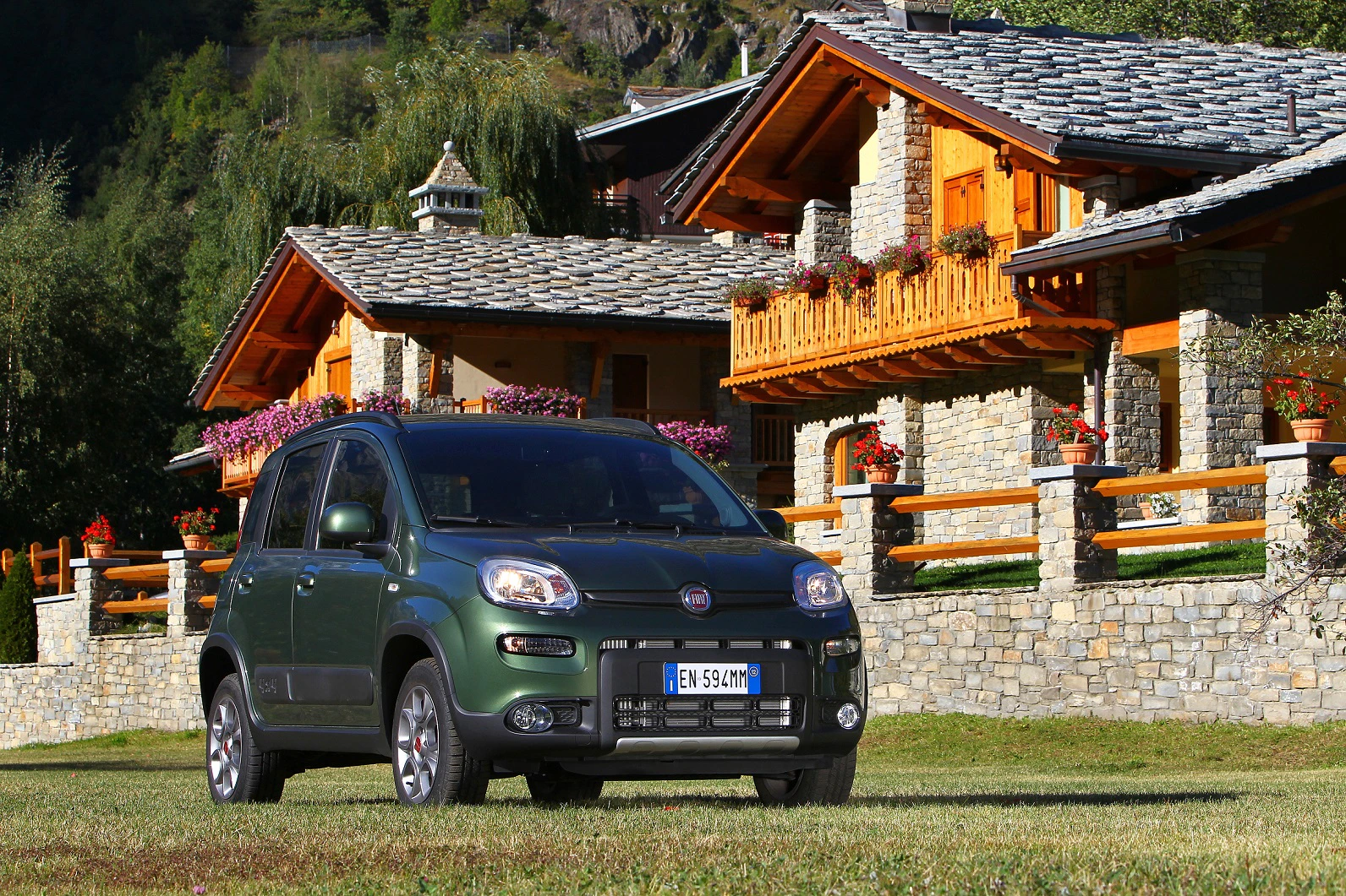 Grüner Fiat Panda parkt vor einem steinernen Chalet mit Holzbalkonen in einer malerischen Berglandschaft.