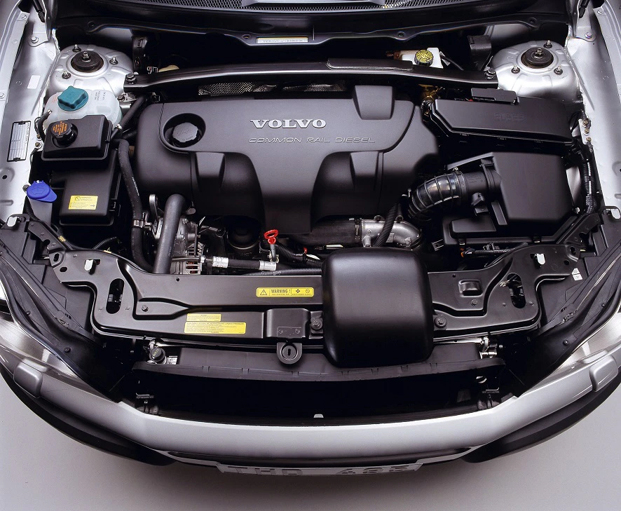 Motorraum eines Volvo-Autos mit Common Rail Diesel-Motor, klar erkennbar durch das Volvo-Logo. Verschiedene Autoteile und Kabel sind sichtbar.