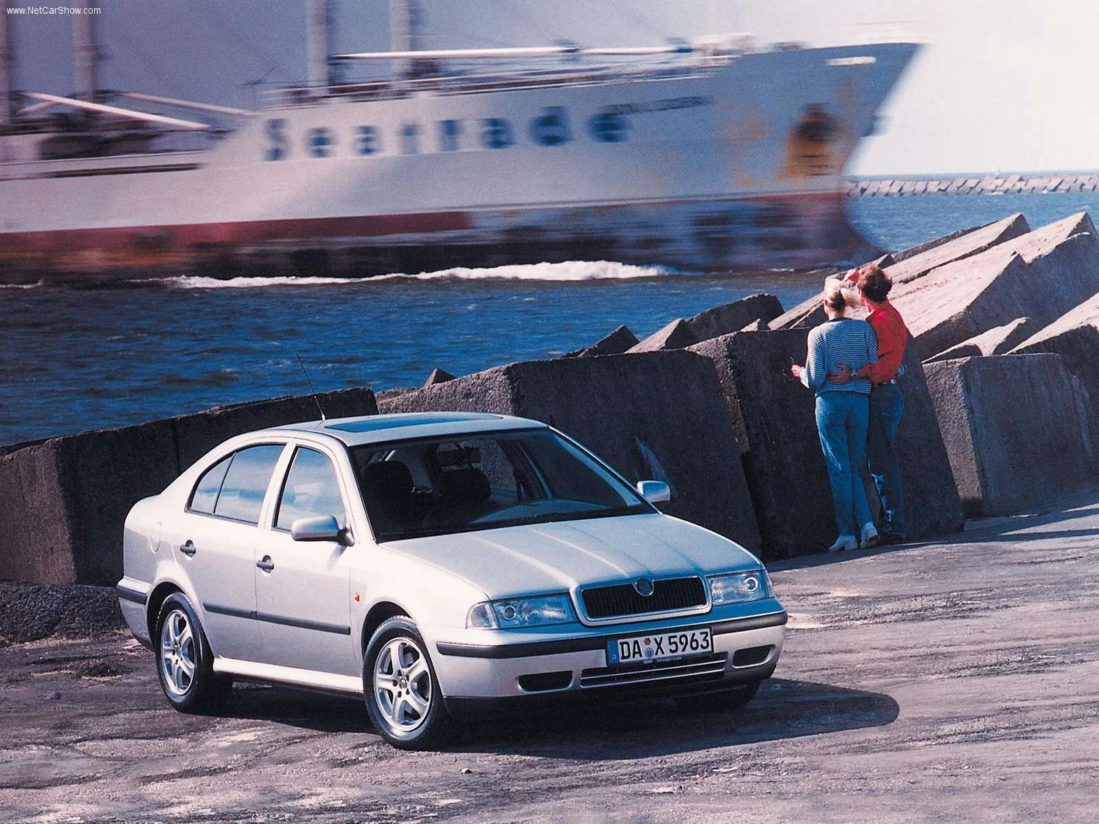 Silberner Skoda Octavia vor Küstenhintergrund mit Paar auf Felsen; Schiff im Hintergrund.