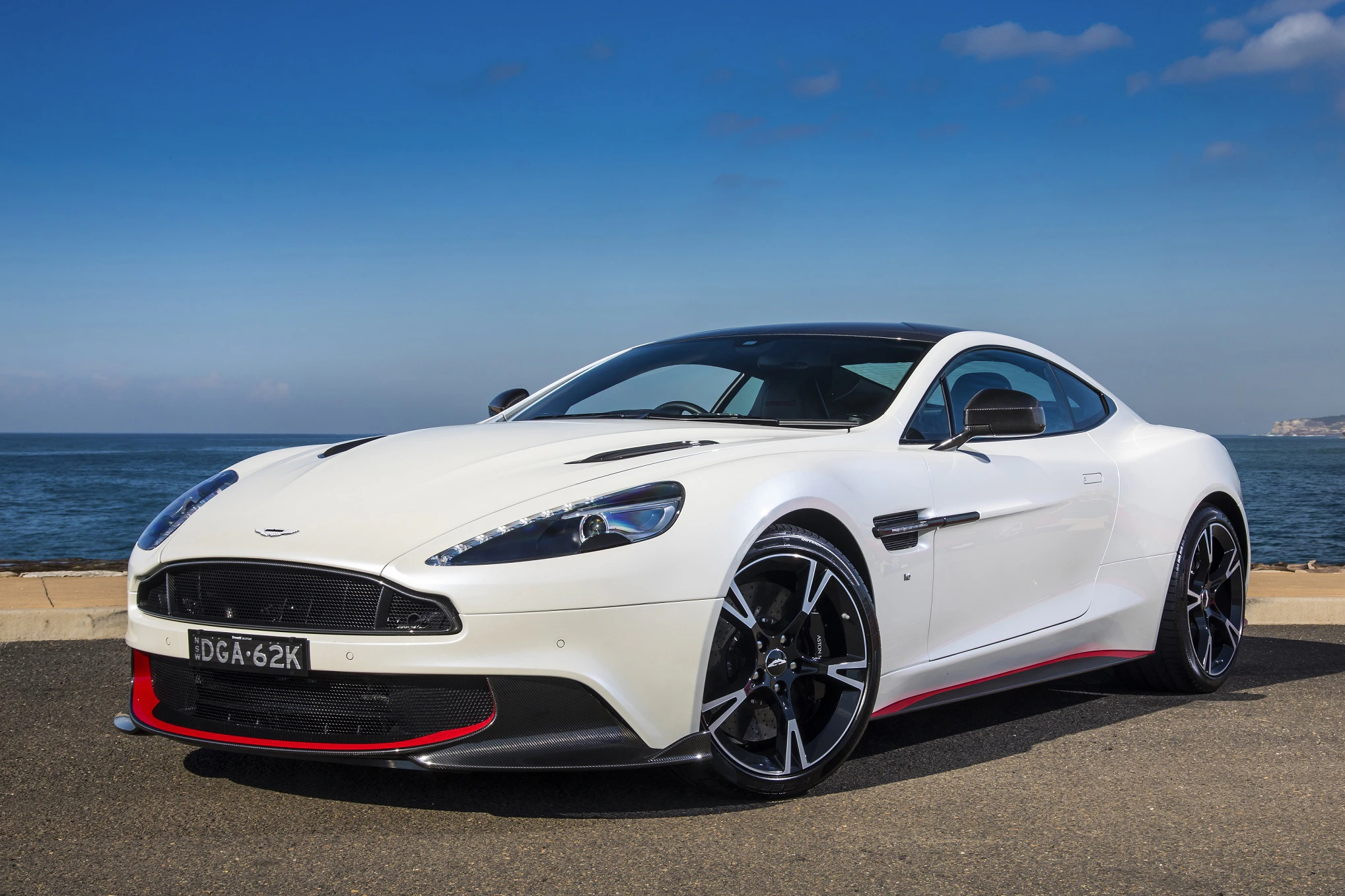 Weißes Sportcoupé am Meer mit blauen Himmel, roten Akzenten und schwarzen Felgen. Im Hintergrund Wasser und Küstenlinie.