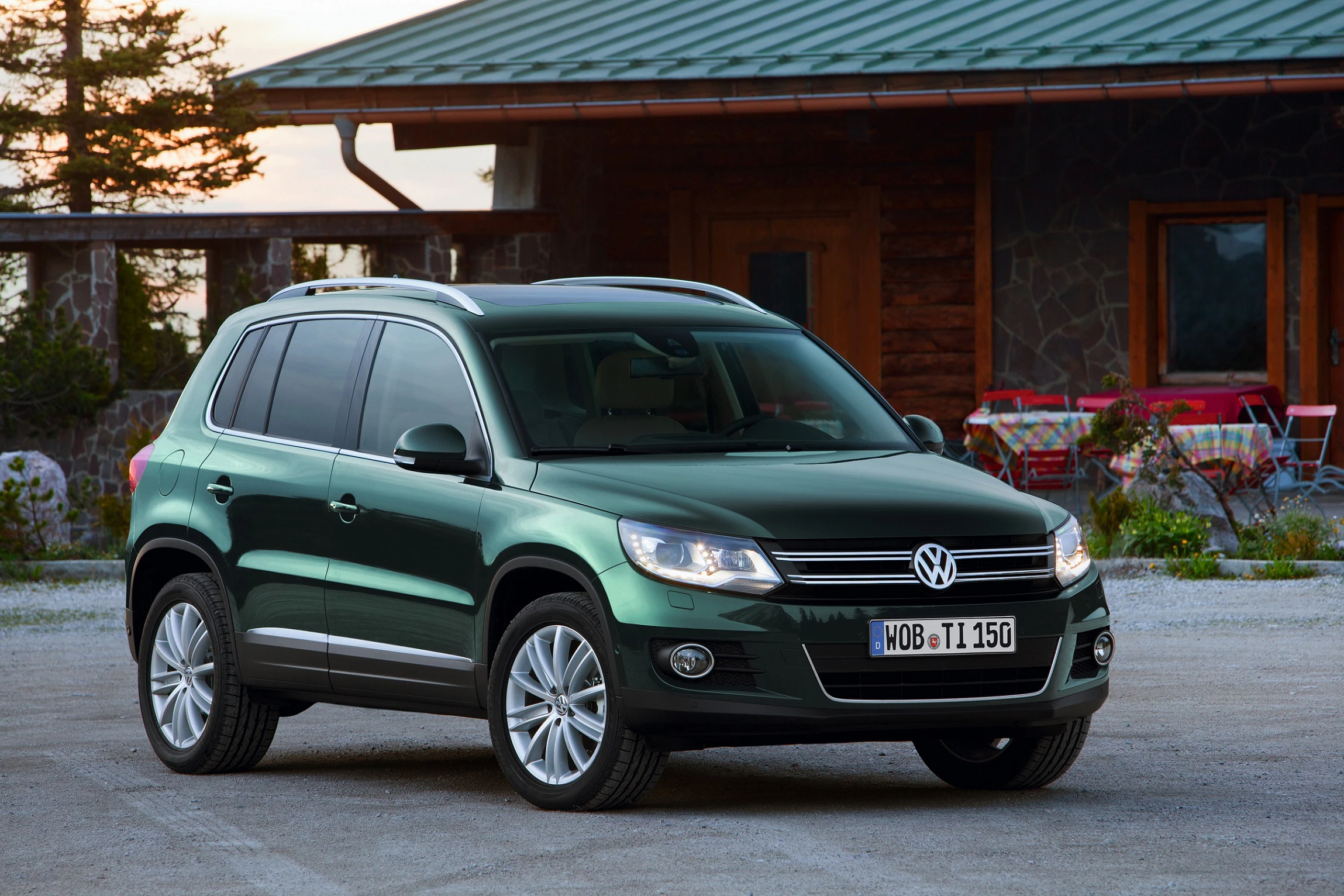 Ein grüner Volkswagen-SUV steht vor einem Haus mit Holzelementen. Der Wagen ist auf einem Schotterplatz geparkt.