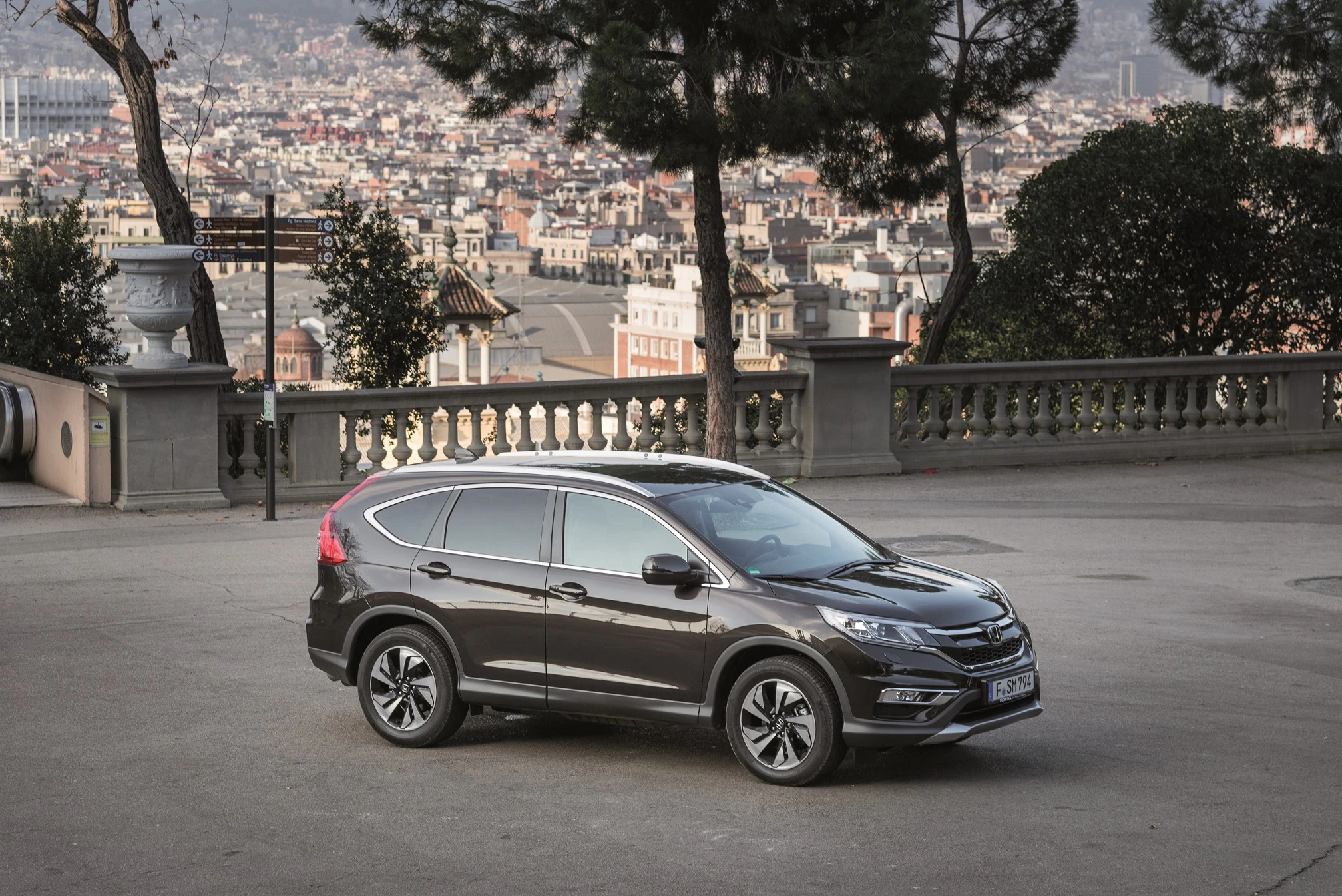 Ein grauer SUV parkt auf einem Platz mit Blick über eine Stadtlandschaft. Im Hintergrund sind Bäume und Gebäude sichtbar.