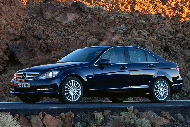 Schwarzer Mercedes-Benz auf Straße, felsige Landschaft im Hintergrund, beleuchtet von warmem Sonnenlicht. Fahrzeug profilansicht.