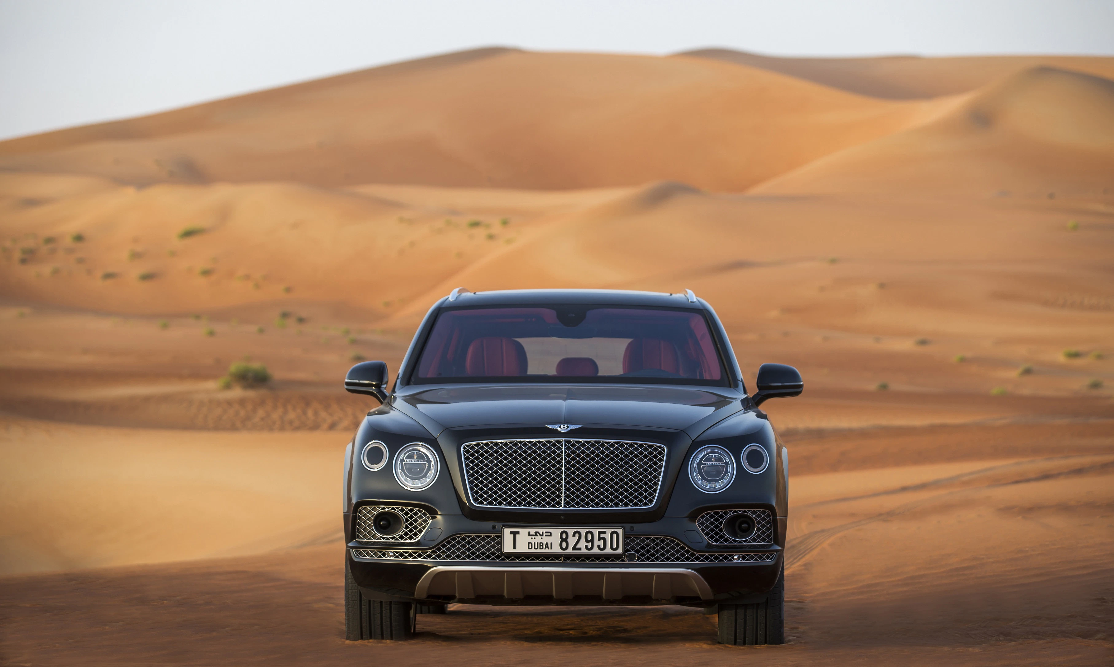 Luxuriöser schwarzer SUV fährt durch eine weite Wüstenlandschaft mit sanften Sanddünen im Hintergrund.