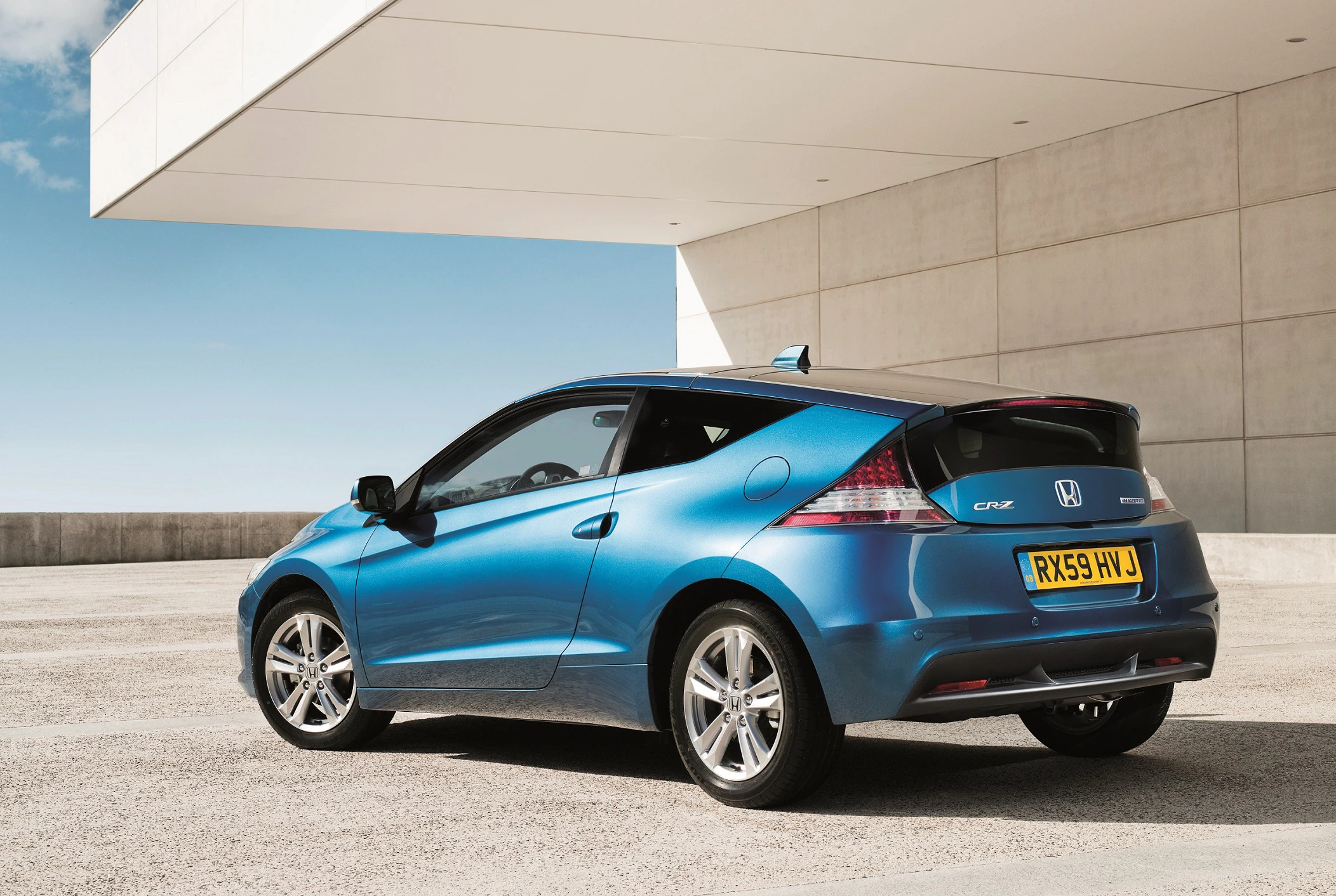 Blauer Honda CR-Z auf einem Parkplatz, Seitenansicht. Modernes Design mit sportlichen Linien vor einem Gebäude und klarem Himmel.