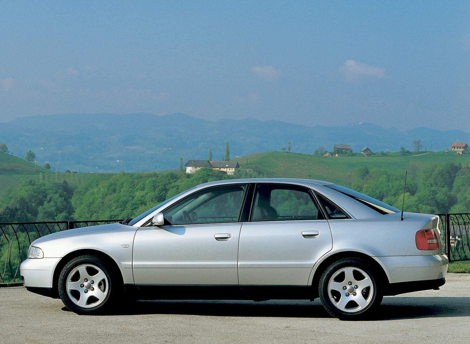 Silberner Audi A4 Limousine steht auf einer Straße vor einer malerischen Landschaft mit grünen Hügeln und blauen Himmel im Hintergrund.