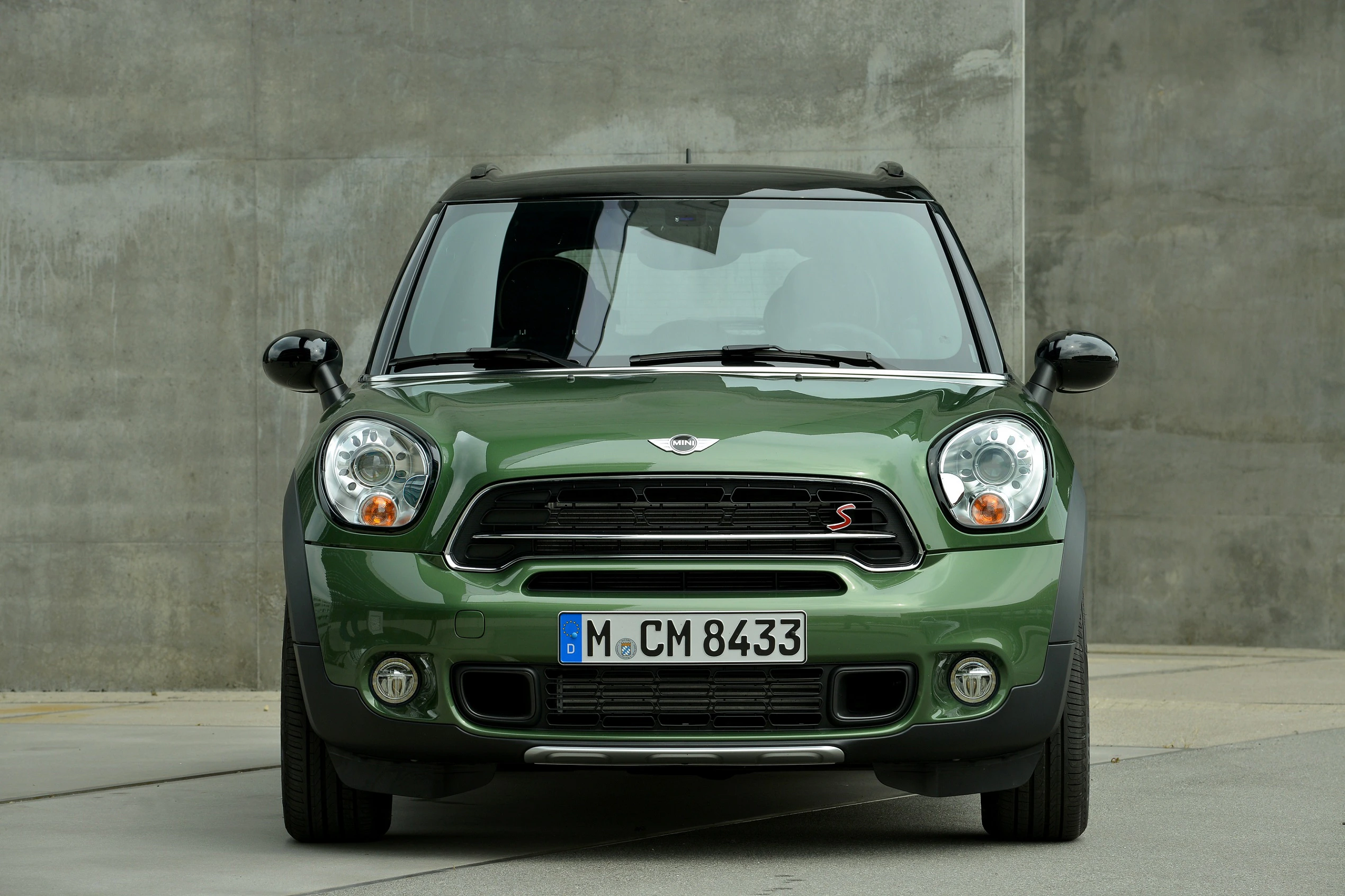 Grüner Mini Cooper S Countryman steht vor einer grauen Betonwand, frontal aufgenommen.
