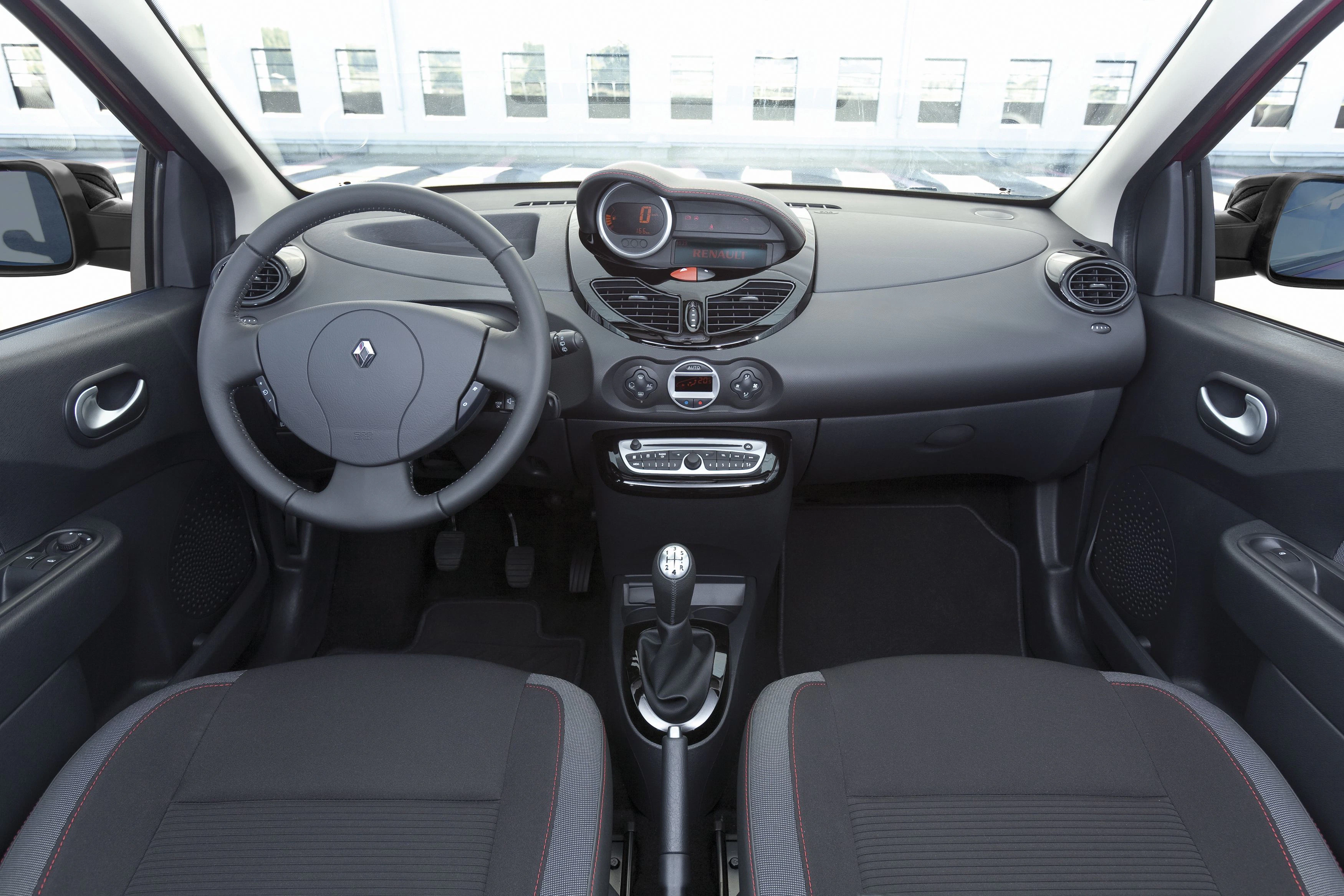 Innenraum eines Autos mit modernem Armaturenbrett, schwarzem Lenkrad, Schalthebel und zwei Vordersitzen in grauem Stoff.