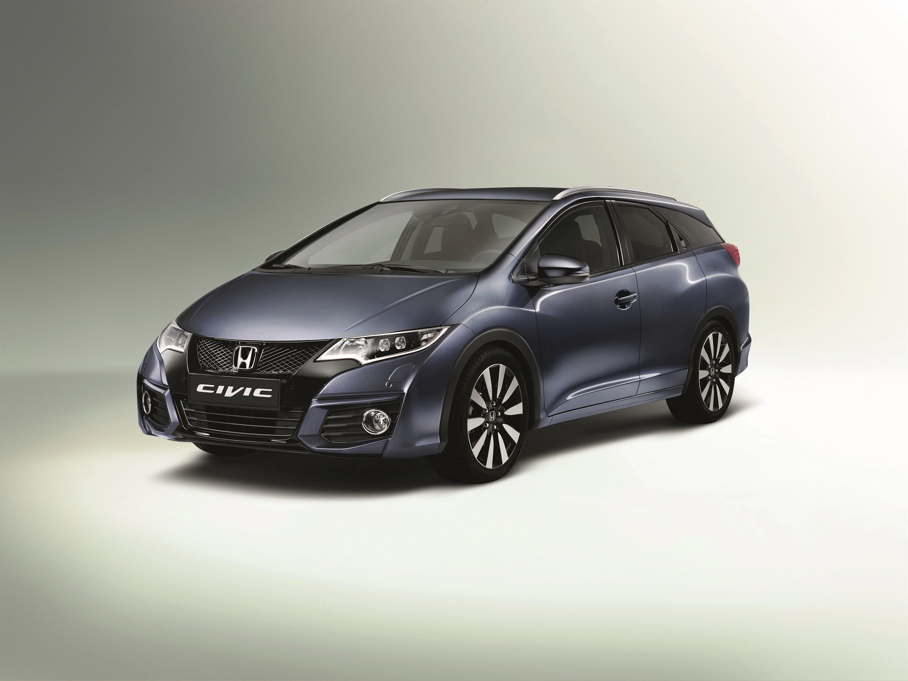 Dunkelgrauer Honda Civic Kombi vor hellem Hintergrund, seitliche Frontansicht mit markanten Scheinwerfern und sportlichem Design.