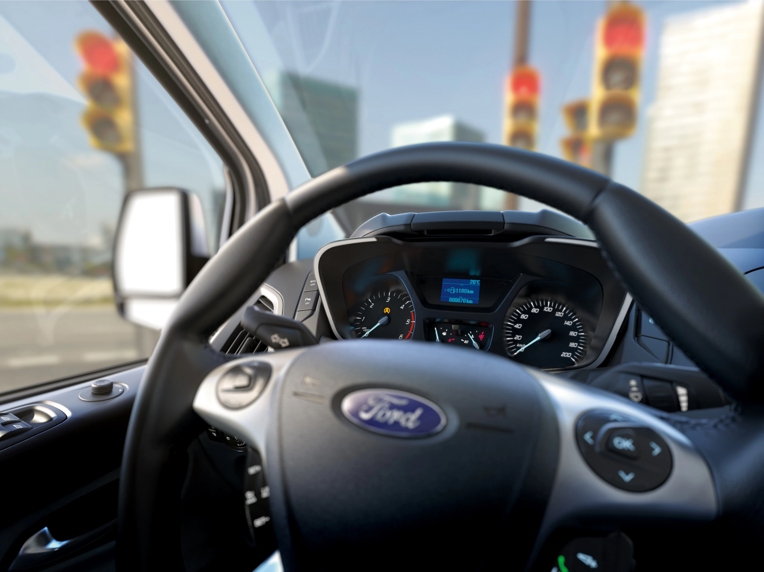 Lenkrad und Armaturenbrett eines Ford-Autos, mit verschwommenem Blick auf Ampeln und städtische Gebäude durch die Windschutzscheibe.