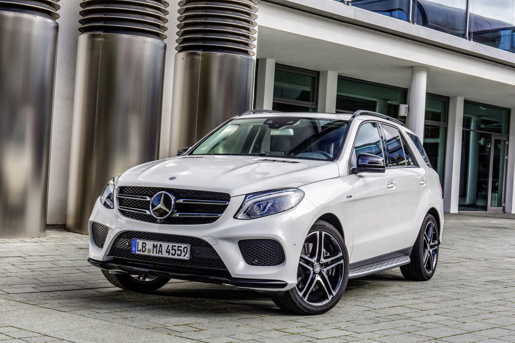 Weißer Mercedes-Benz SUV parkt vor einem modernen Gebäude mit Glasfront und metallischen Säulen.