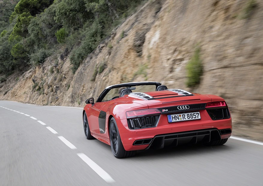 Roter Audi R8 Spyder fährt auf kurviger Bergstraße entlang einer Felswand, umgeben von Bäumen.
