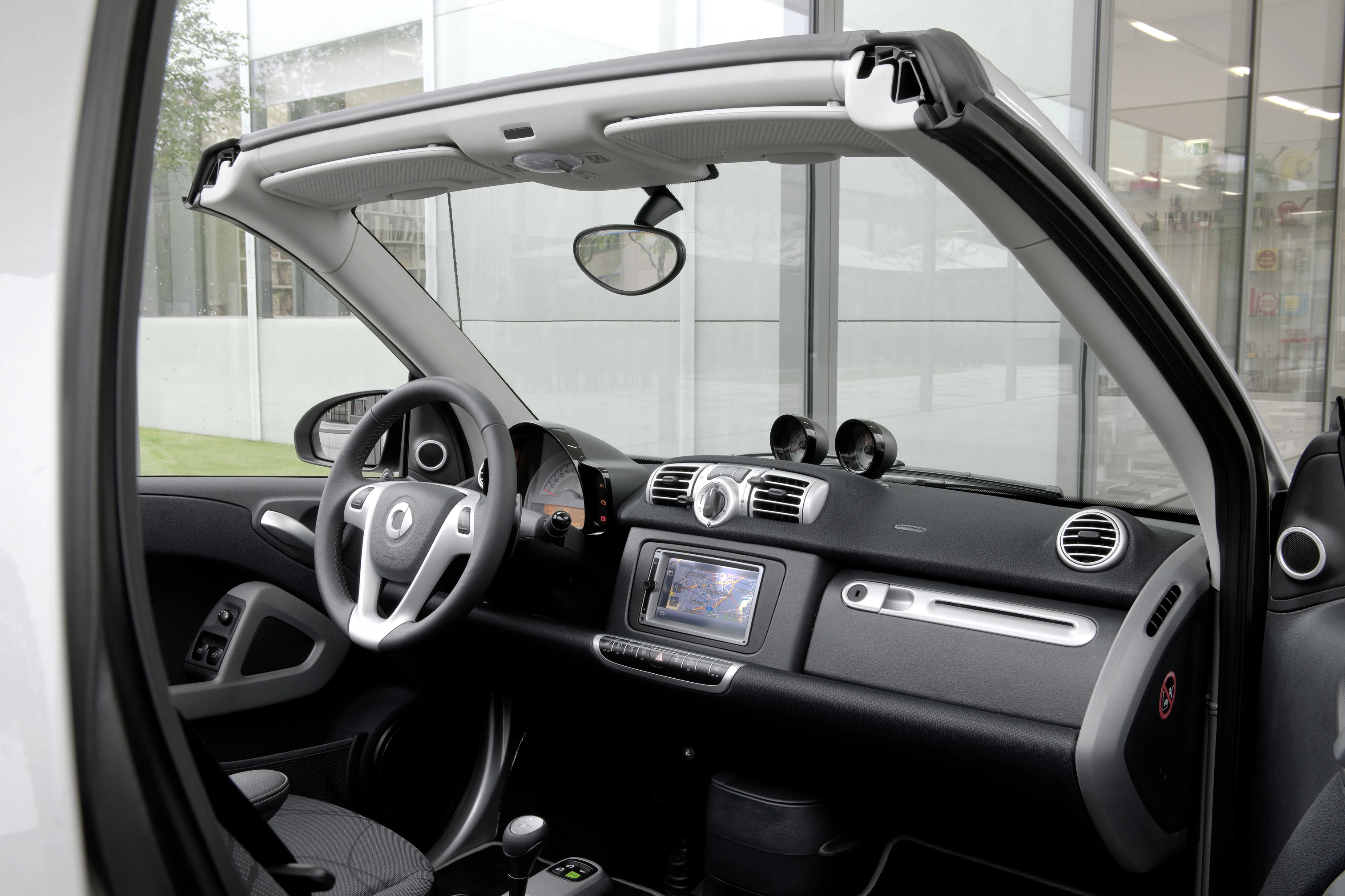 Innenraum eines Autos mit offenem Dach, modernen Armaturen und Lenkrad; Fokus auf Navigationseinheit und minimalistisches Design.