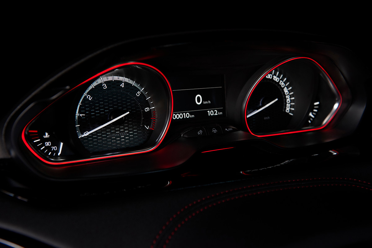 Nahaufnahme eines beleuchteten Tachometers und Drehzahlmessers in einem Auto, mit leuchtend roten Rändern auf schwarzem Hintergrund.