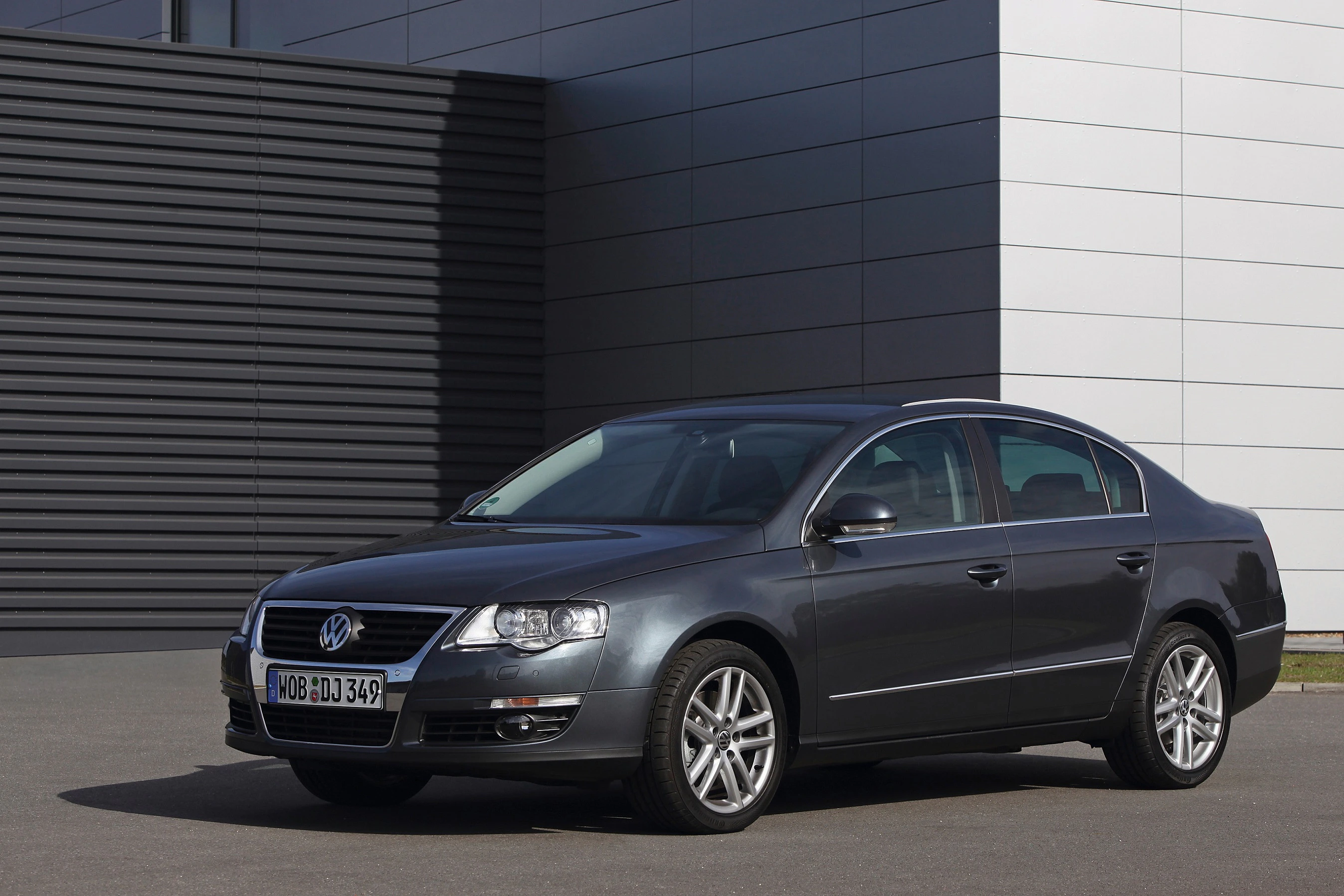 Grauer Volkswagen Passat-Limousine parkt vor einem modernen Gebäude mit horizontaler und vertikaler Fassadenverkleidung.