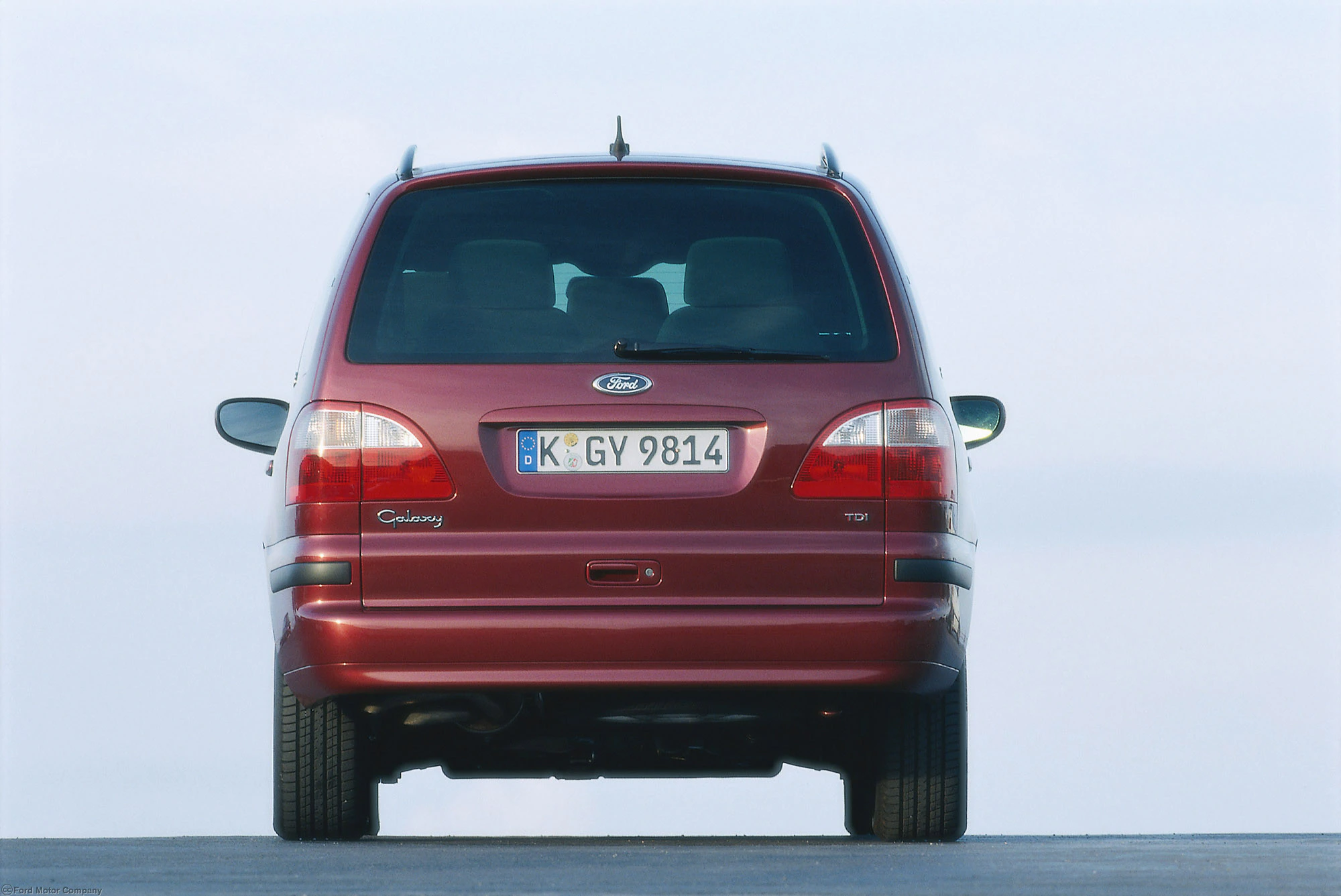 Roter Ford Galaxy von hinten auf freier Fläche, mit deutschem Kennzeichen "K-GY 9814", blauer Himmel im Hintergrund.