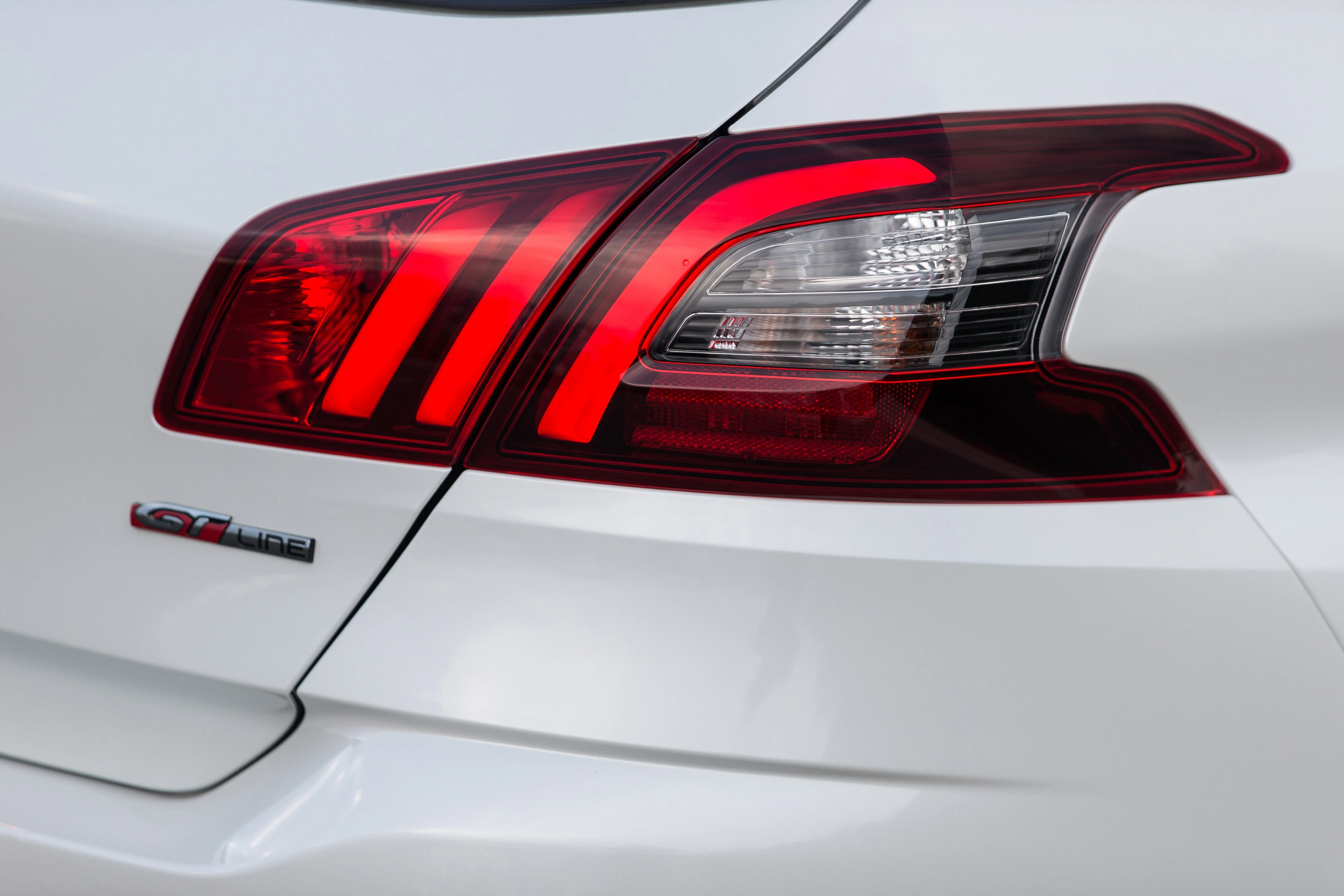 Nahaufnahme eines weißen Autos mit rot beleuchtetem Rücklicht und GT-Line-Emblem, das moderne Designakzente setzt.