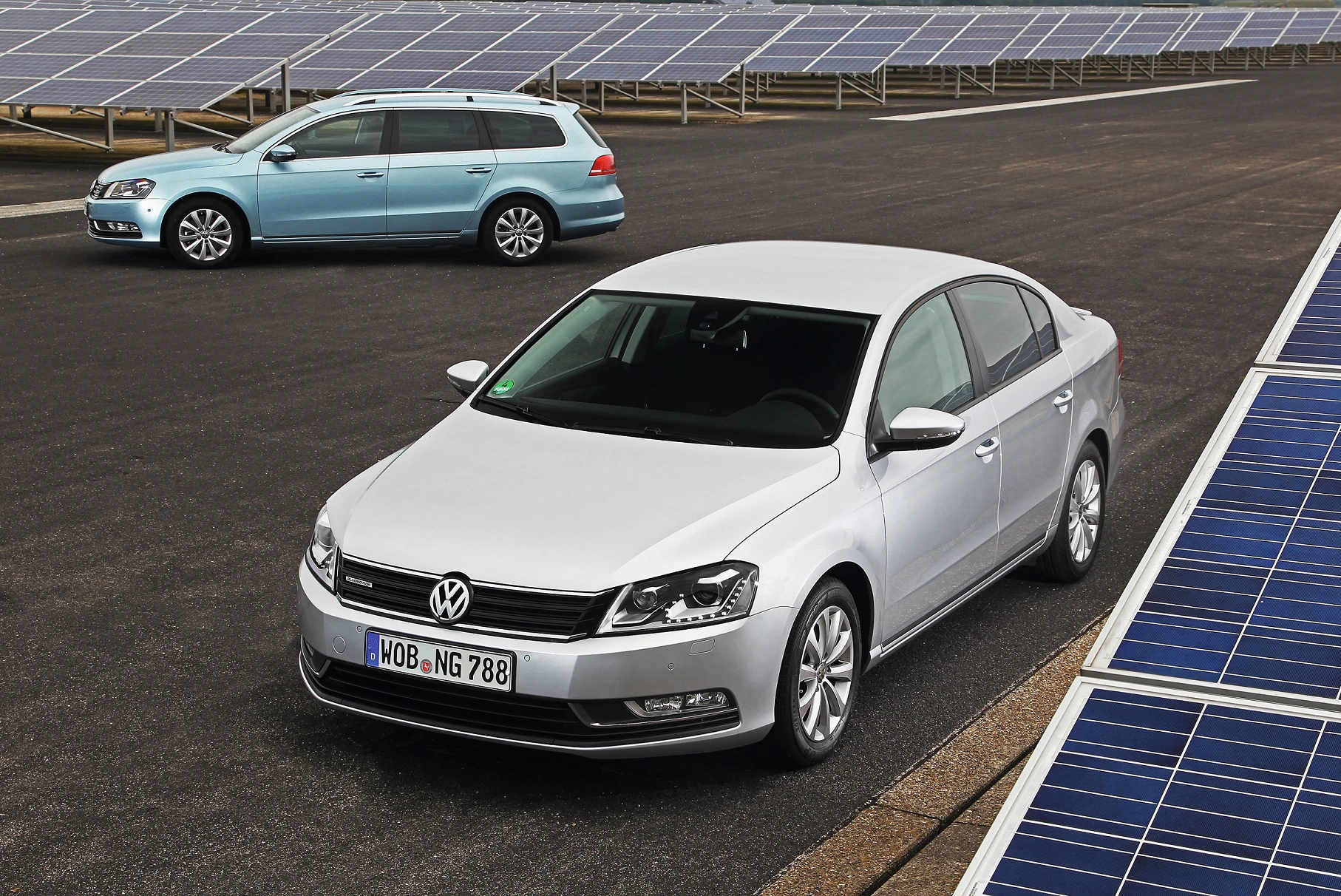 Zwei VW-Passats, einer silbern und einer hellblau, parken auf einem Parkplatz neben Solarmodulen.