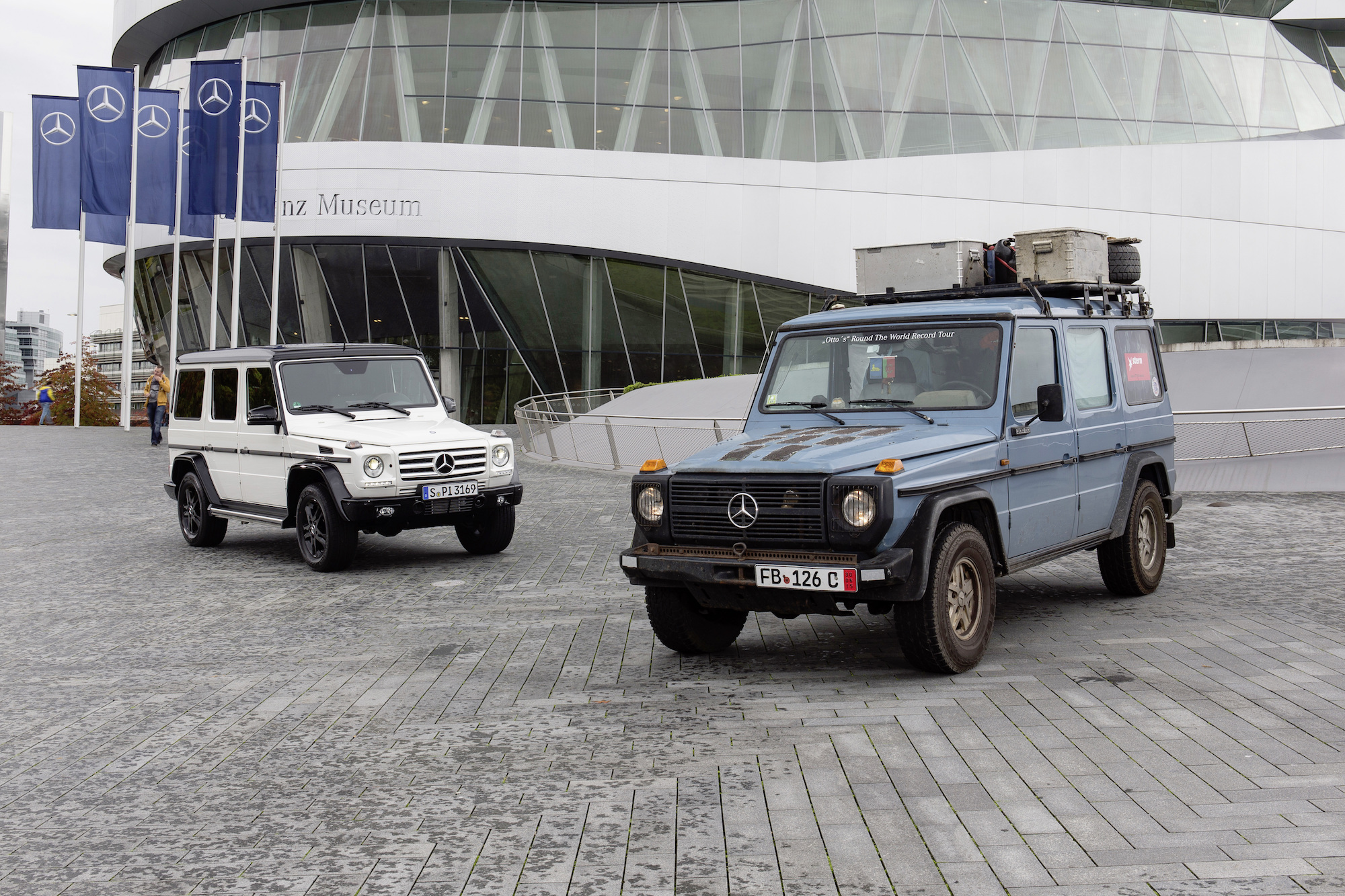 Zwei Mercedes Geländewagen vor dem Mercedes-Benz Museum, einer in Weiß und der andere in Blau mit Dachgepäckträger.