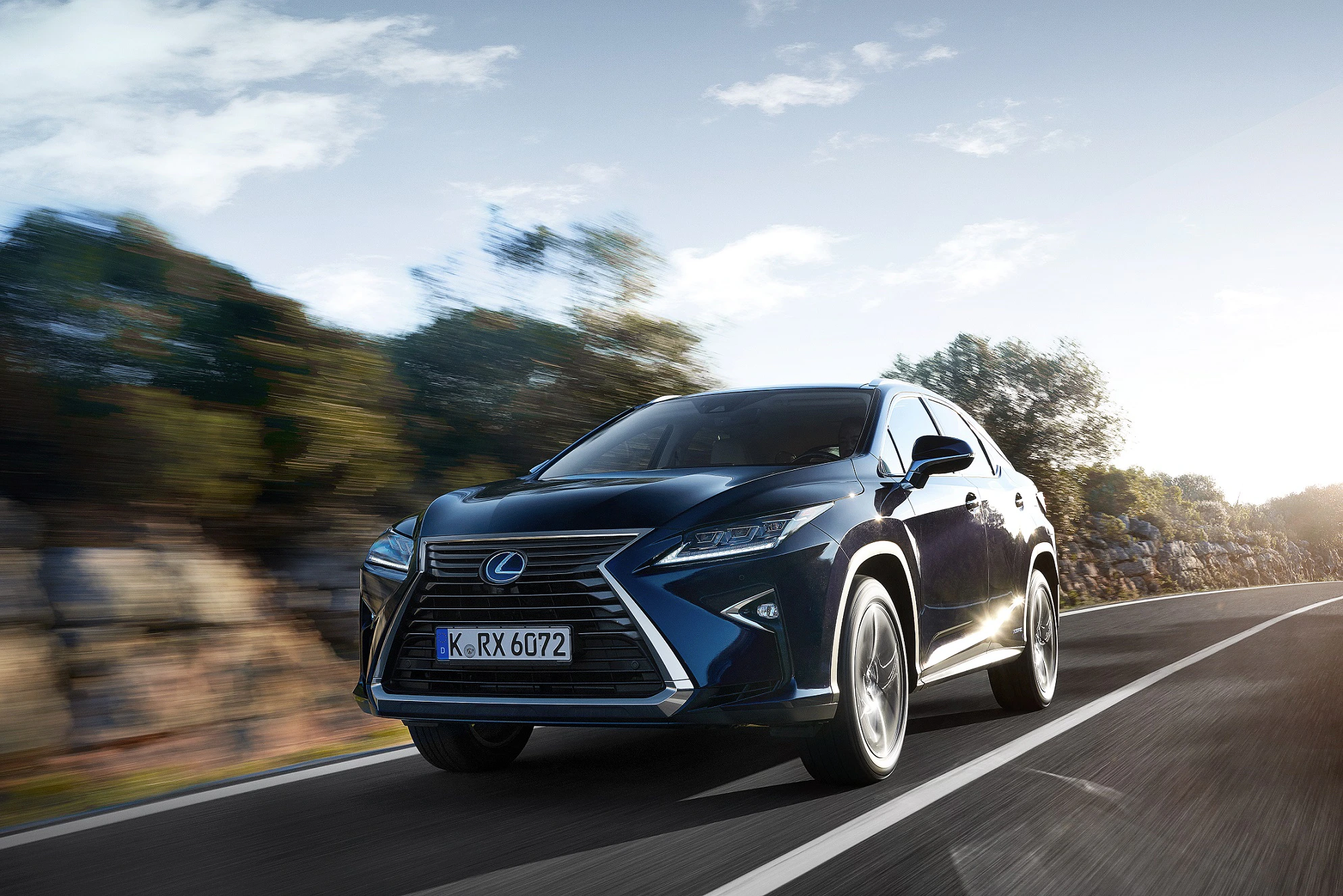 Ein schwarzer Lexus SUV fährt auf einer Landstraße bei Tageslicht, umgeben von unscharfen Bäumen und blauem Himmel.