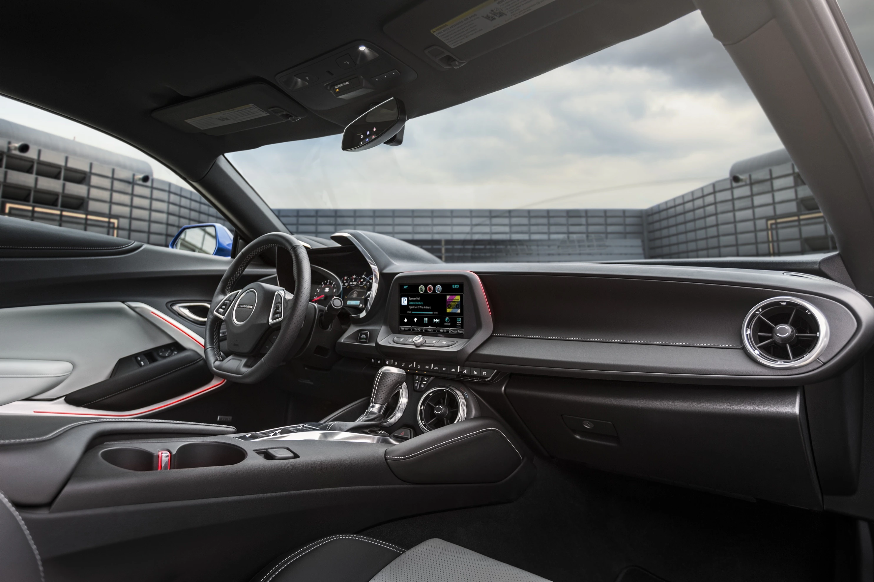 Innenraum eines modernen Autos mit Ledersitzen, Lenkrad, Touchscreen-Display und Mittelkonsole. Draußen sind Wolken am Himmel sichtbar.