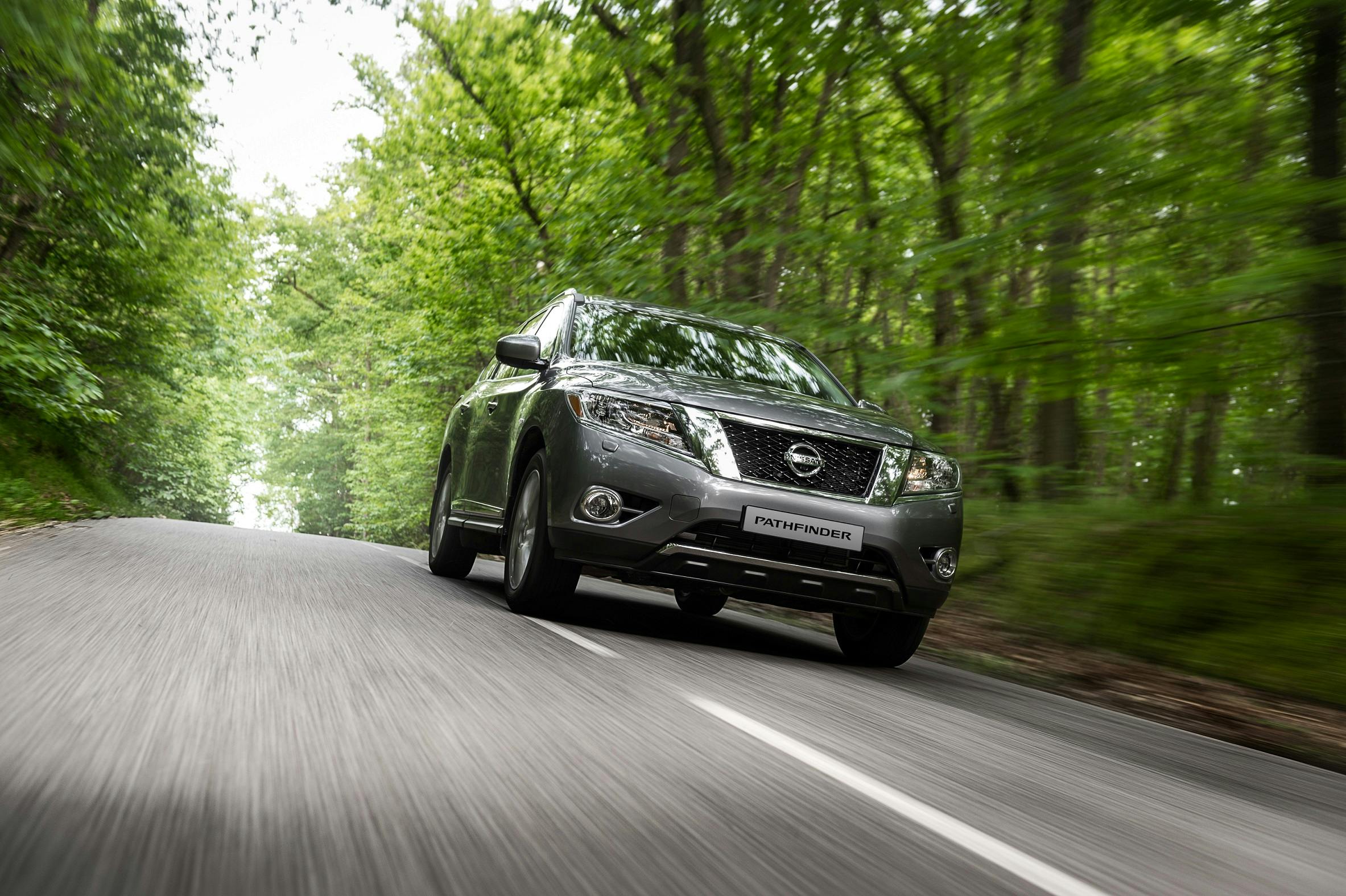 Ein grauer Nissan Pathfinder fährt auf einer kurvenreichen Straße durch einen grünen, bewaldeten Bereich.