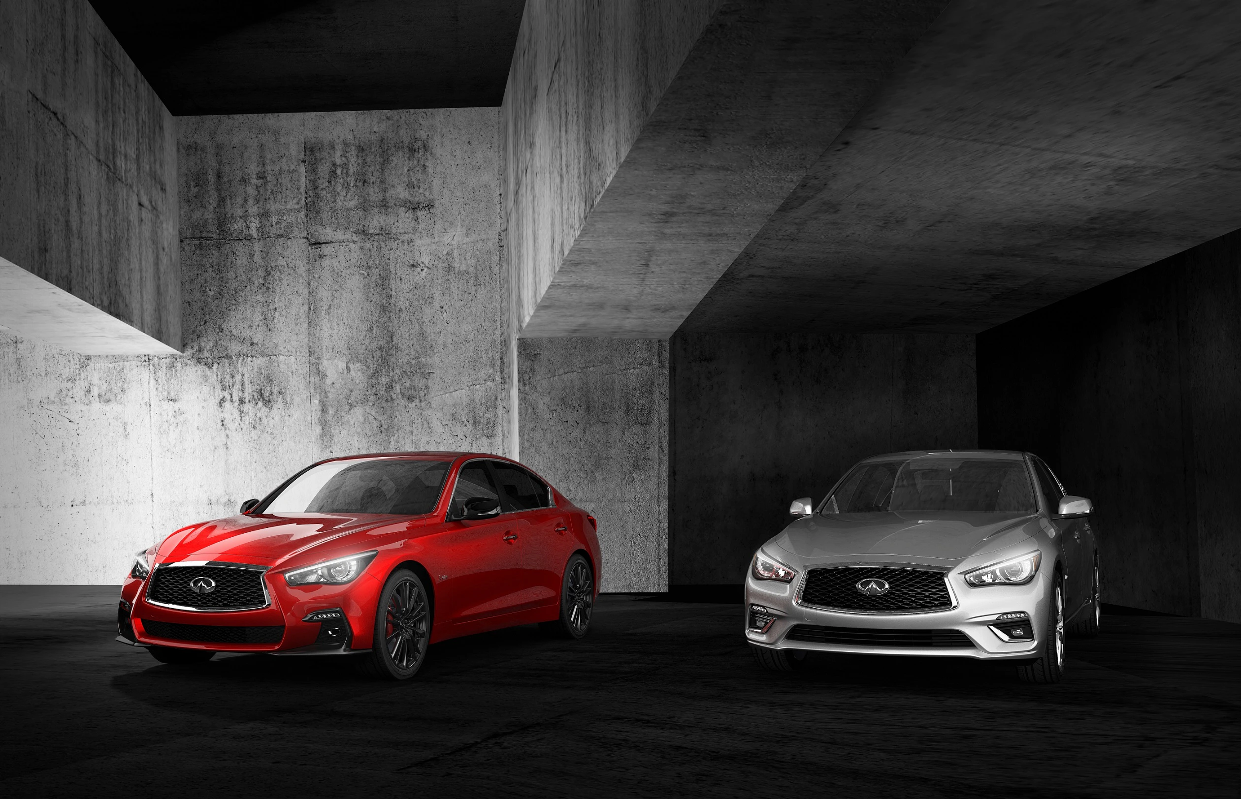 Zwei Infinity-Luxusautos, ein rotes und ein silbernes, stehen in modernem, betonartigem Raum mit markanten geometrischen Formen.