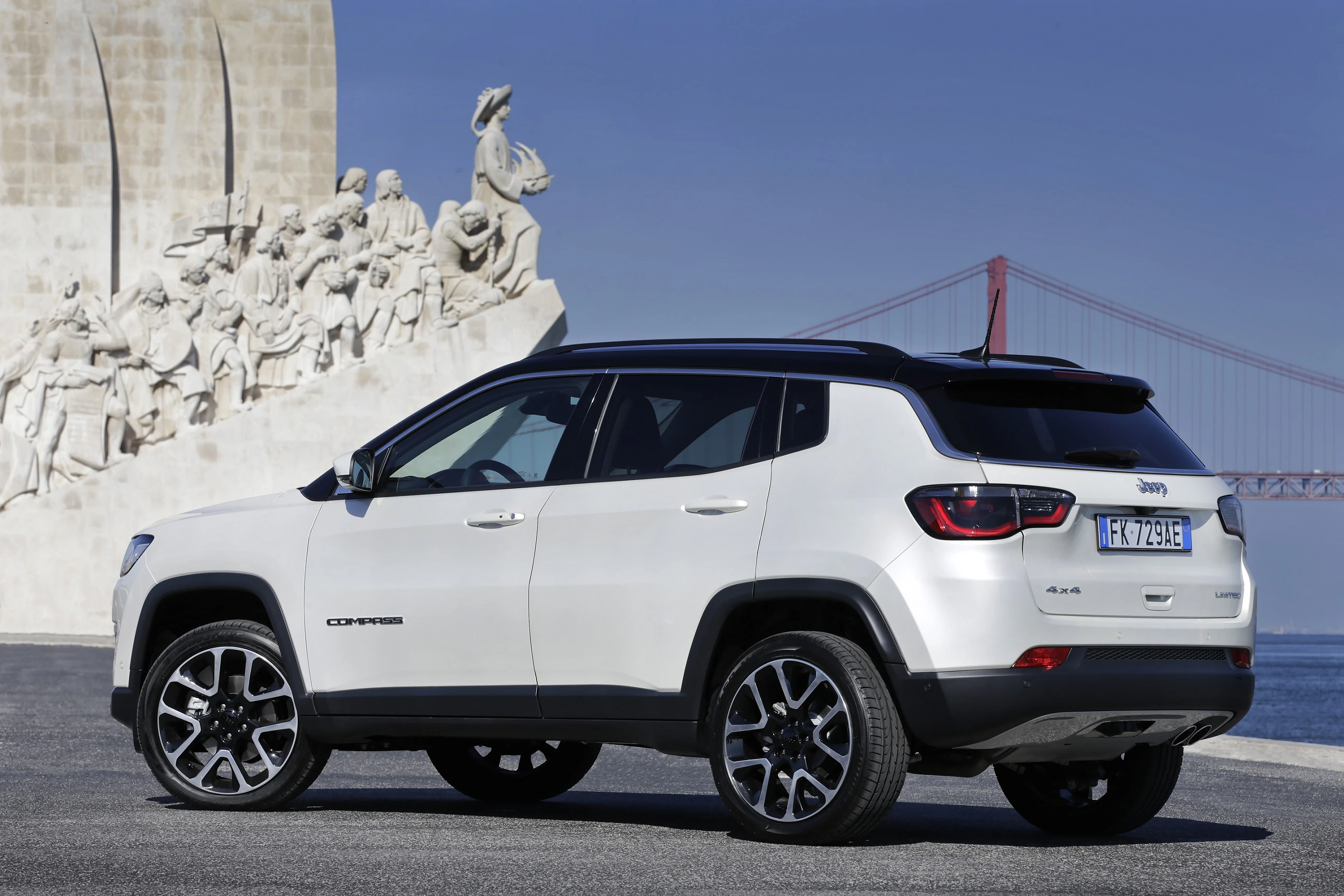 Weißer SUV parkt vor einem historischen Denkmal mit Reliefs. Im Hintergrund ist eine rote Brücke vor einem klaren, blauen Himmel zu sehen.