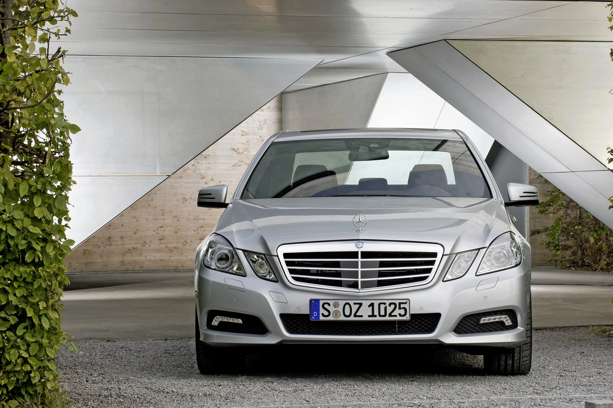 Silberner Mercedes-Benz E-Klasse parkt vor moderner Architektur mit geometrischen Formen und umgebenden Pflanzen.