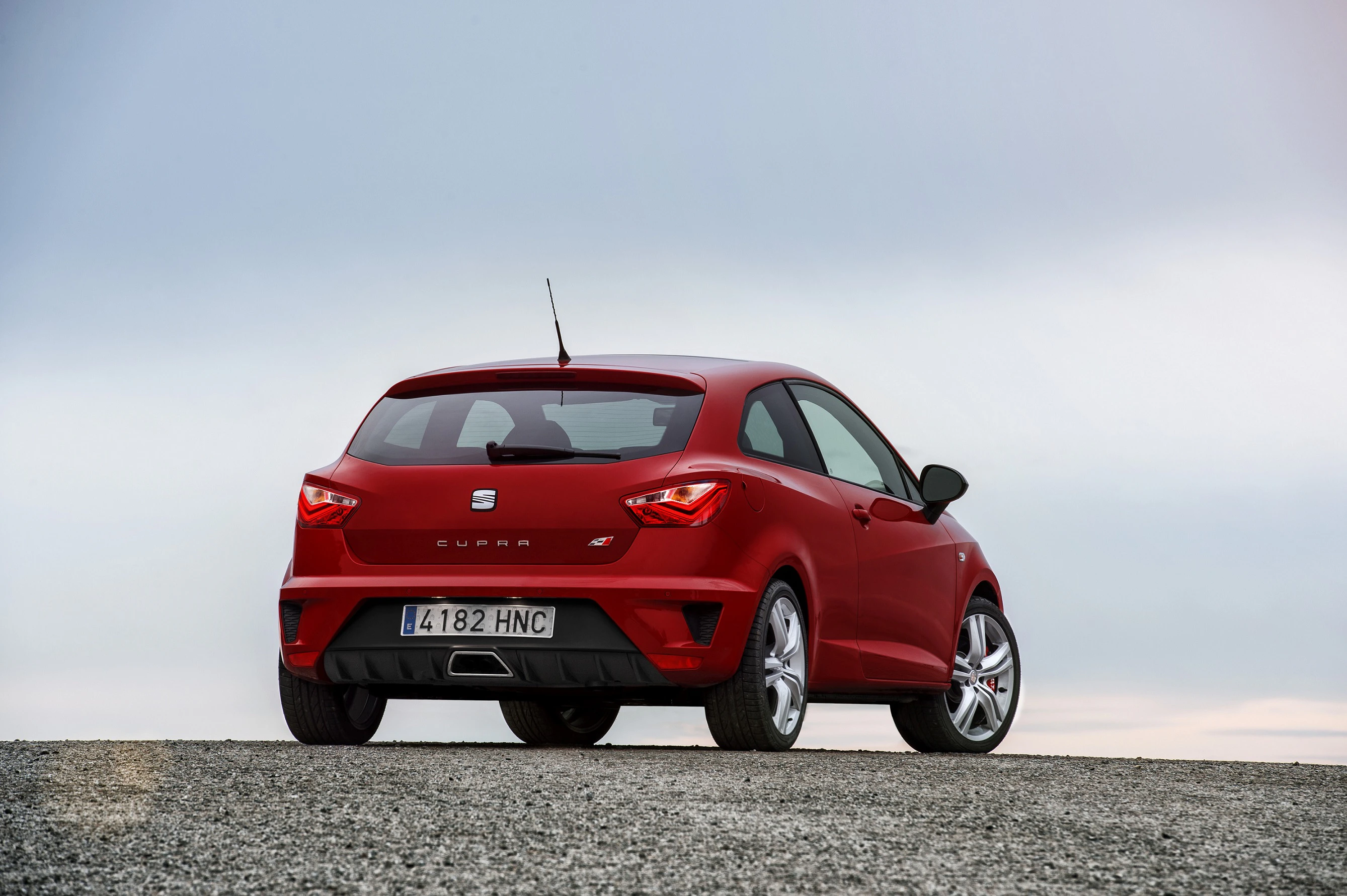 Roter Sportwagen auf grauem Gelände, Heckansicht. Überwiegend bewölkter Himmel. Automodell mit sportlichem Design.