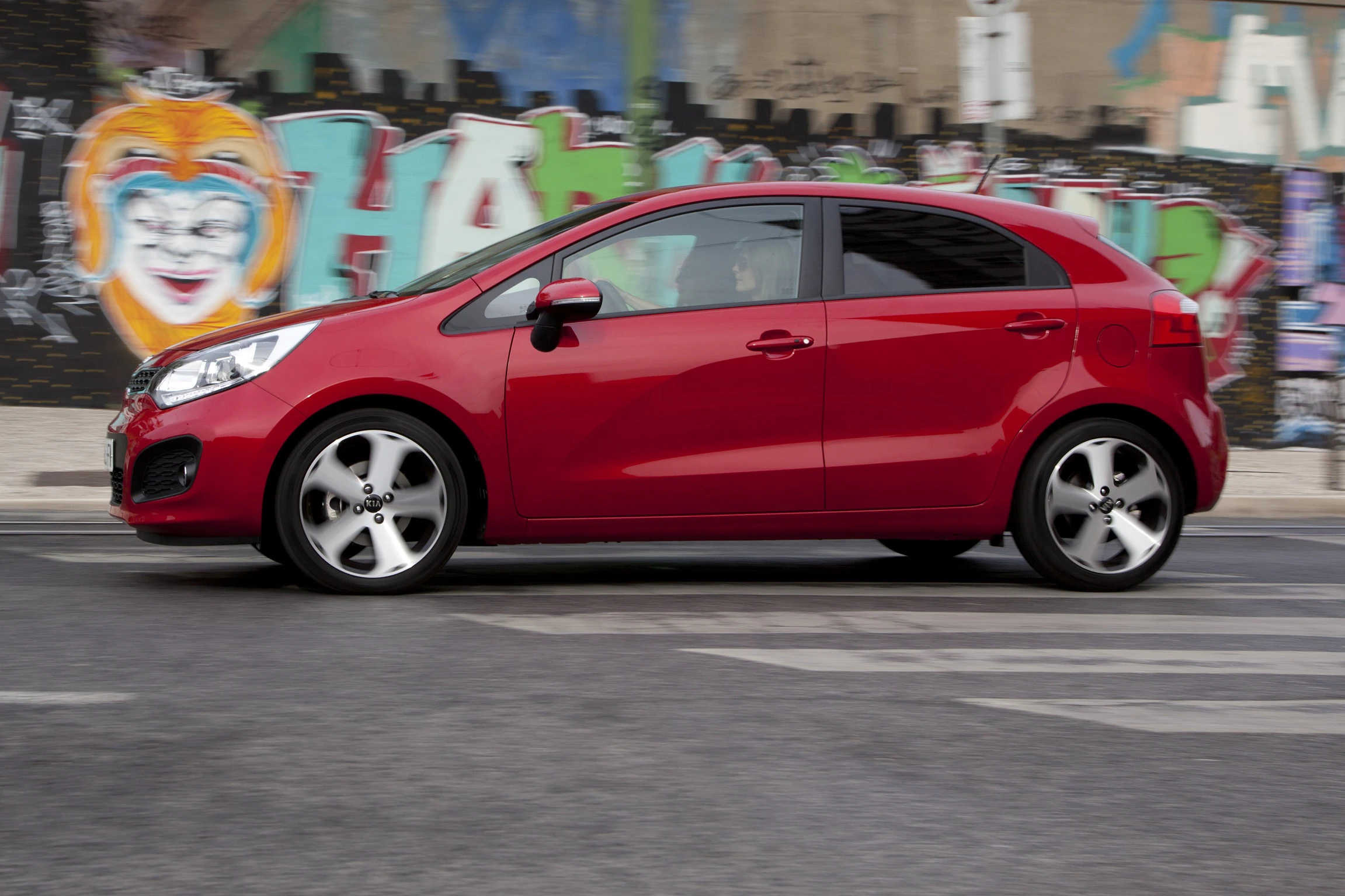 Rotes Auto fährt an bunter Graffiti-Wand vorbei. Modernes Stadtdesign mit kreativem Kunstwerk im Hintergrund.