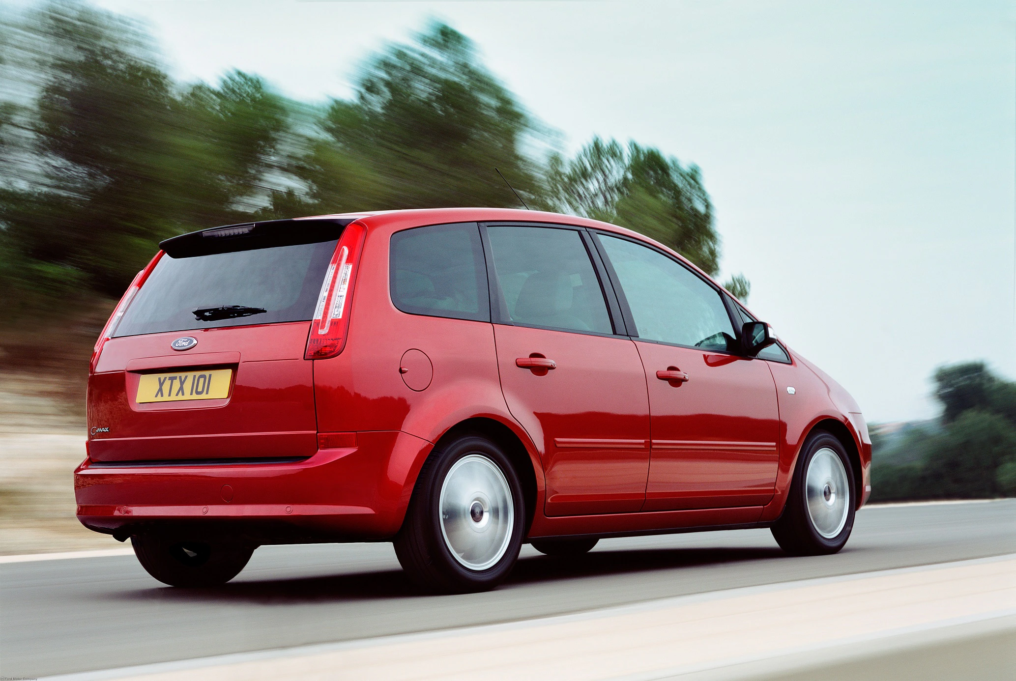 Ein roter Minivan fährt auf einer Landstraße vor einer bewaldeten Kulisse.