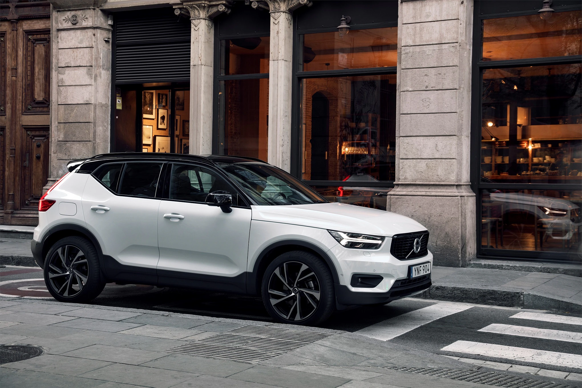 Weißer SUV parkt vor einem Gebäude mit großen Fenstern und Holztüren in einer städtischen Umgebung.