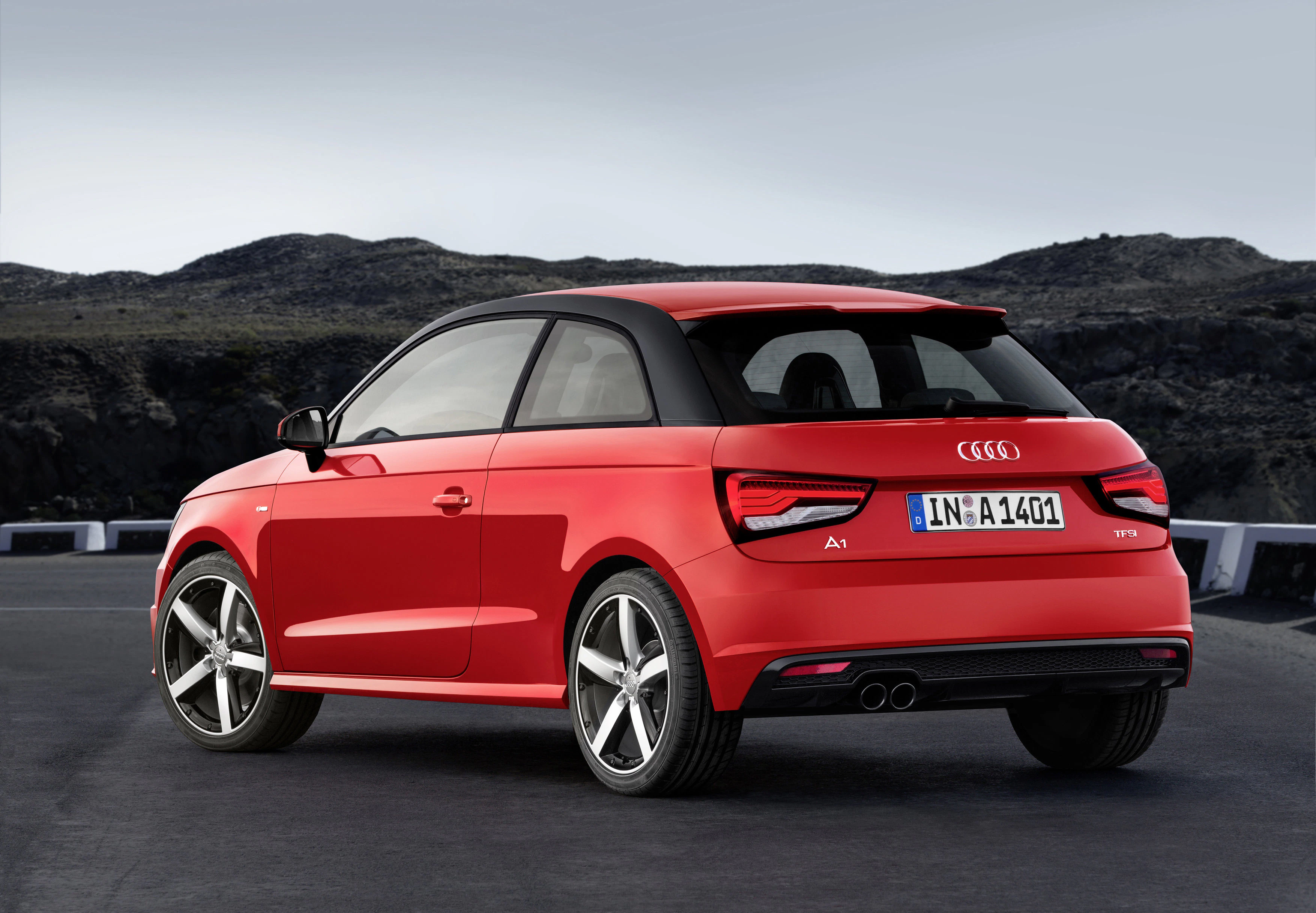 Roter Audi A1 parkt auf einer Straße vor einer dunklen, felsigen Kulisse. Das Auto hat ein schwarzes Dach und silberne Felgen.