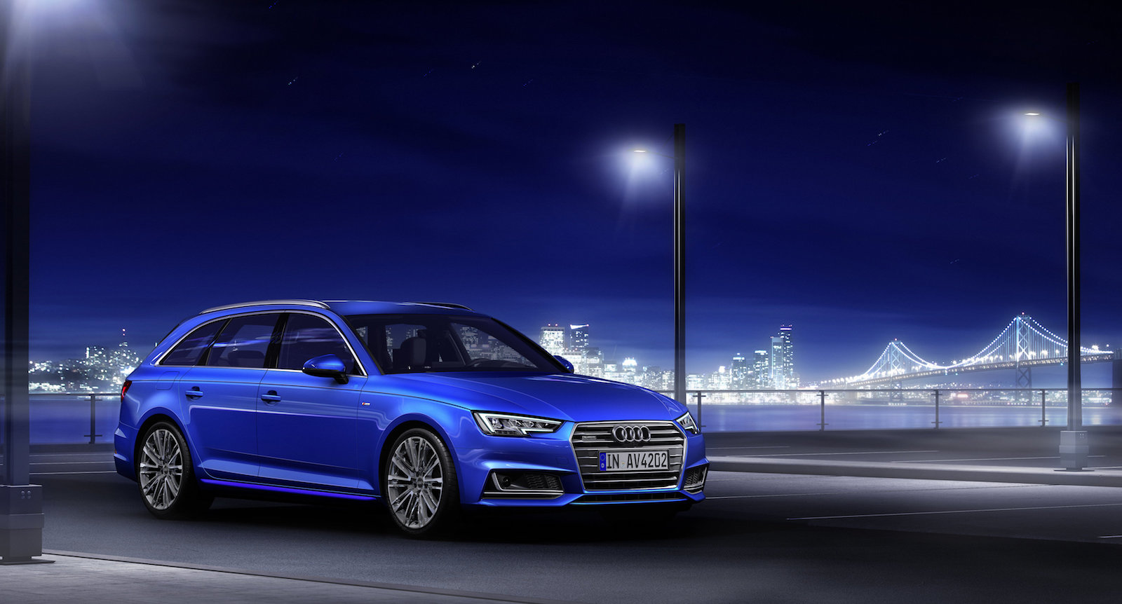 Blauer Audi A4 Avant parkt nachts auf einer beleuchteten Straße, im Hintergrund sind eine erleuchtete Brücke und die Skyline einer Stadt zu sehen.