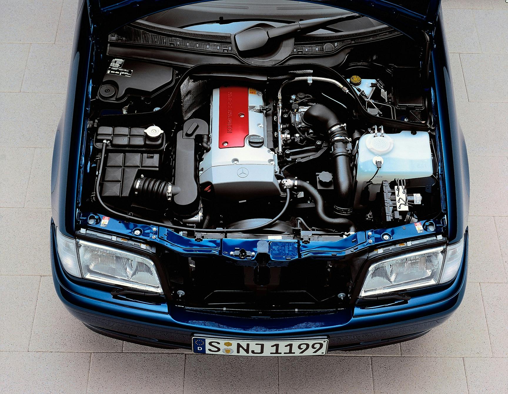 Motorraum eines blauen Autos mit geöffnetem Motorhaube, sichtbar sind Motor, Batterie und diverse Bauteile.