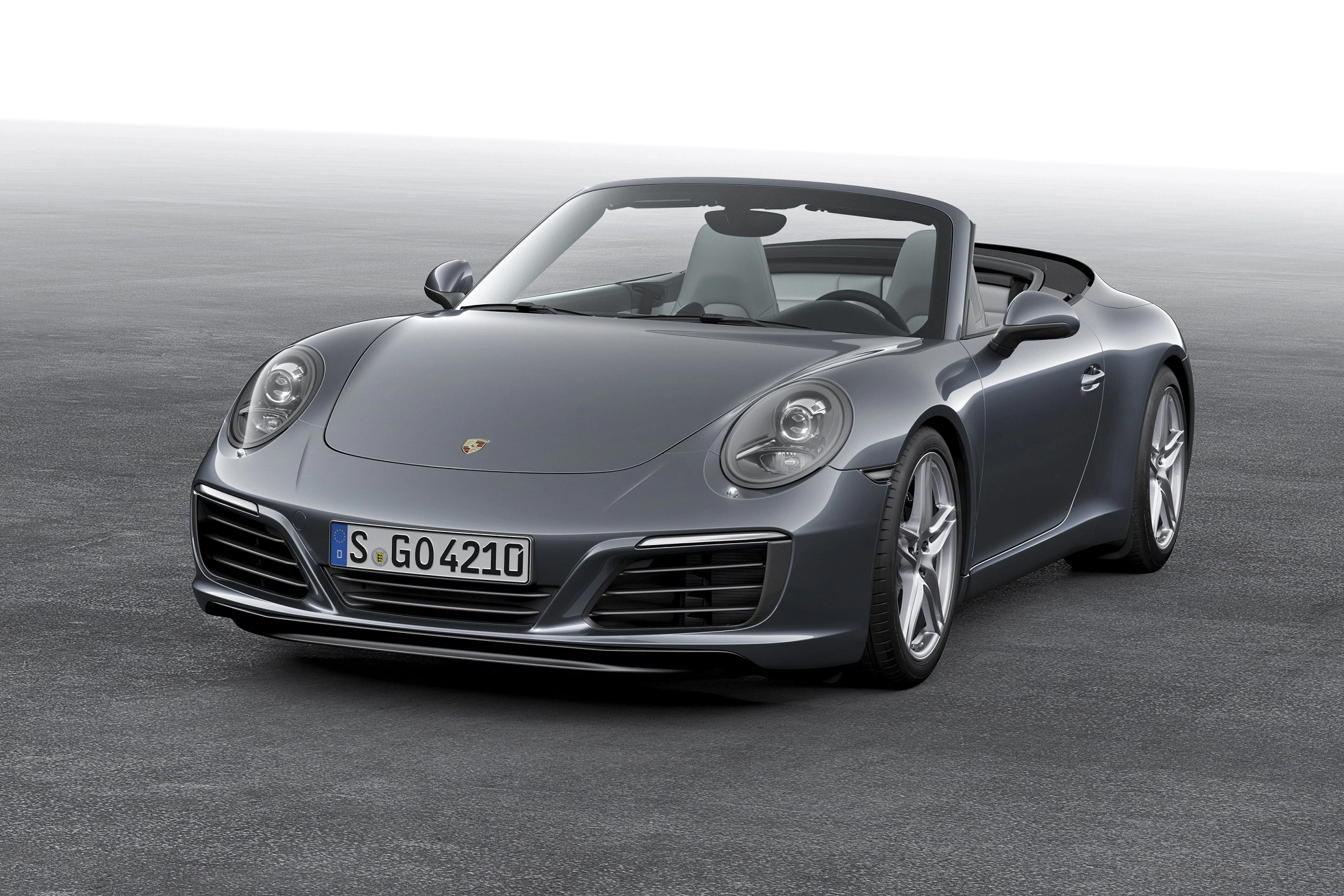 Graues Cabriolet-Sportauto auf einer asphaltierten Fläche, Vorderansicht. Der Himmel ist bewölkt und der Hintergrund ist schlicht.