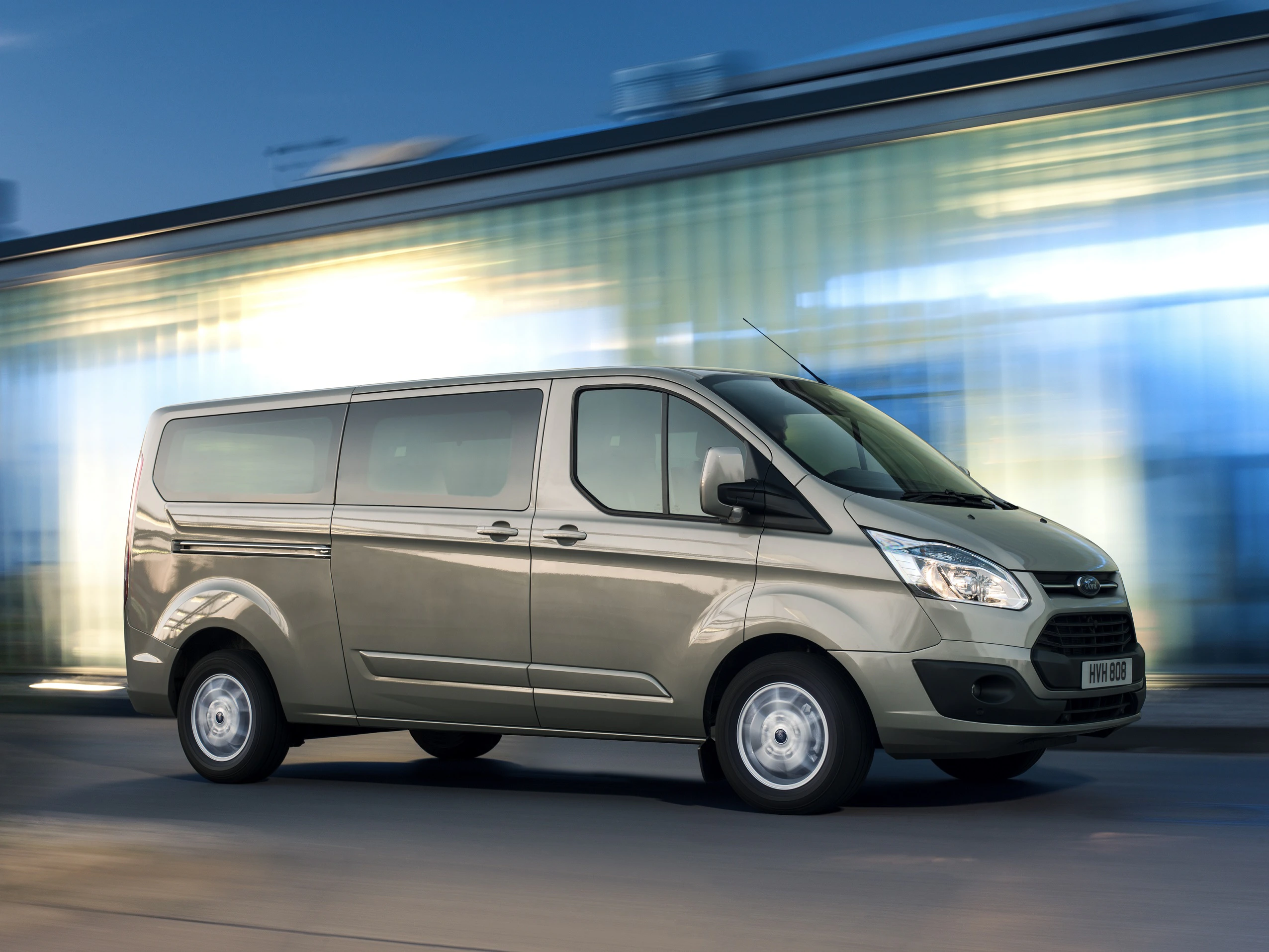 Grauer Minivan fährt dynamisch auf einer Straße mit unscharfem Hintergrund bei Tag.