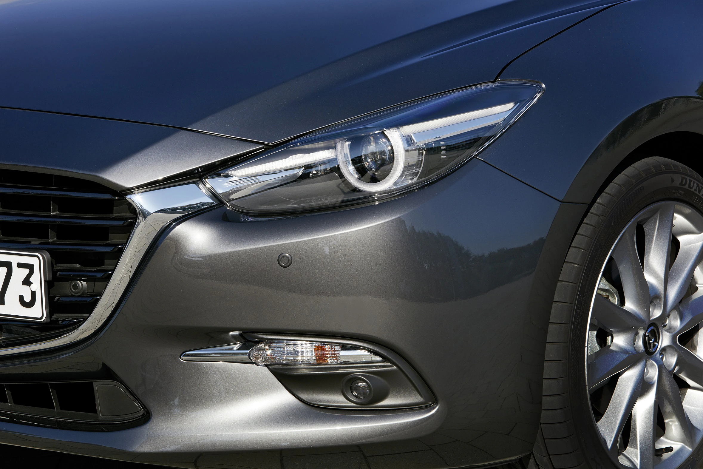 Nahaufnahme eines grauen Autos mit elegantem Frontscheinwerfer und Alufelge. Moderne und sportliche Fahrzeuggestaltung.