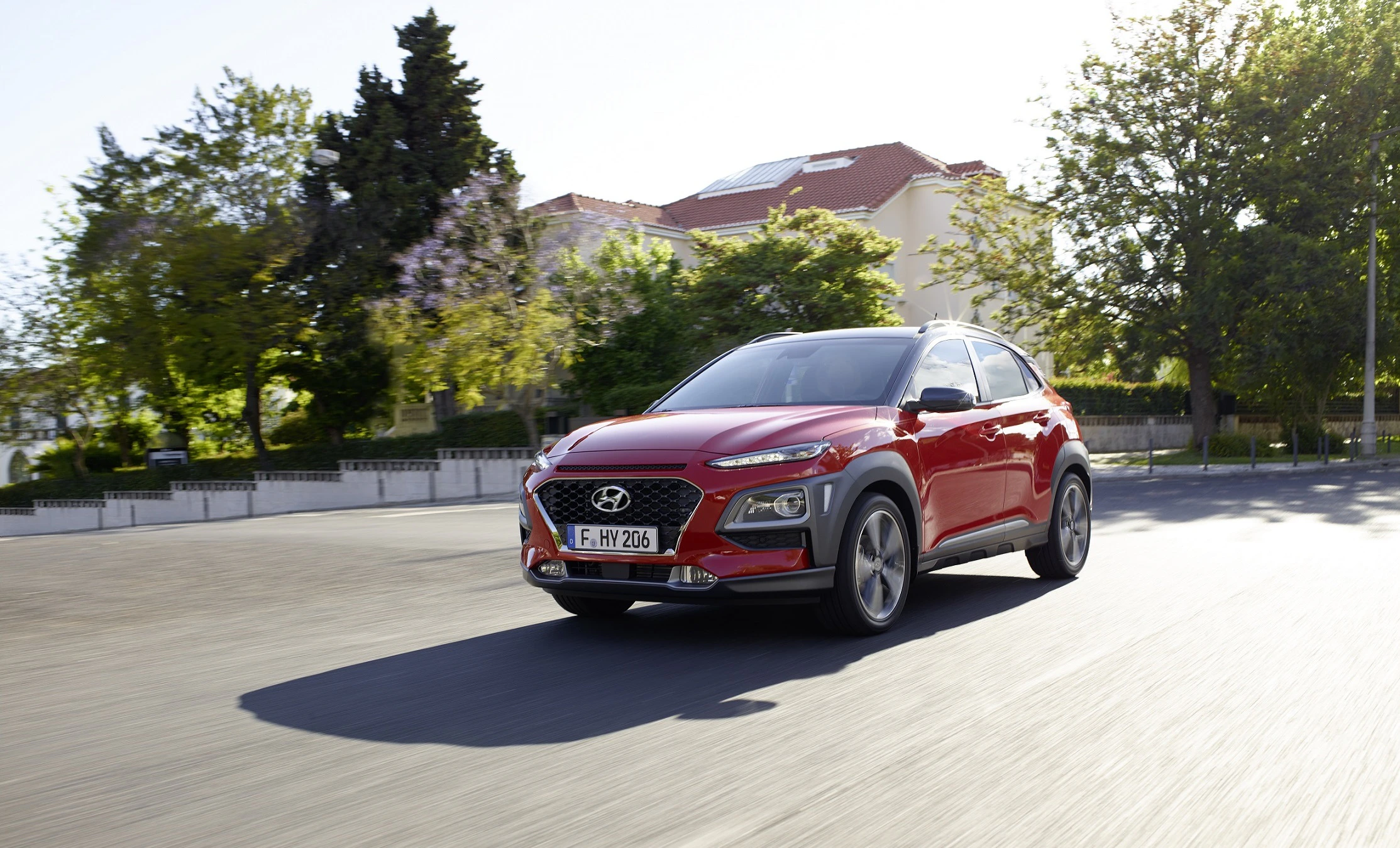 Roter Hyundai SUV fährt auf einer sonnigen Straße, umgeben von Bäumen und Häusern.