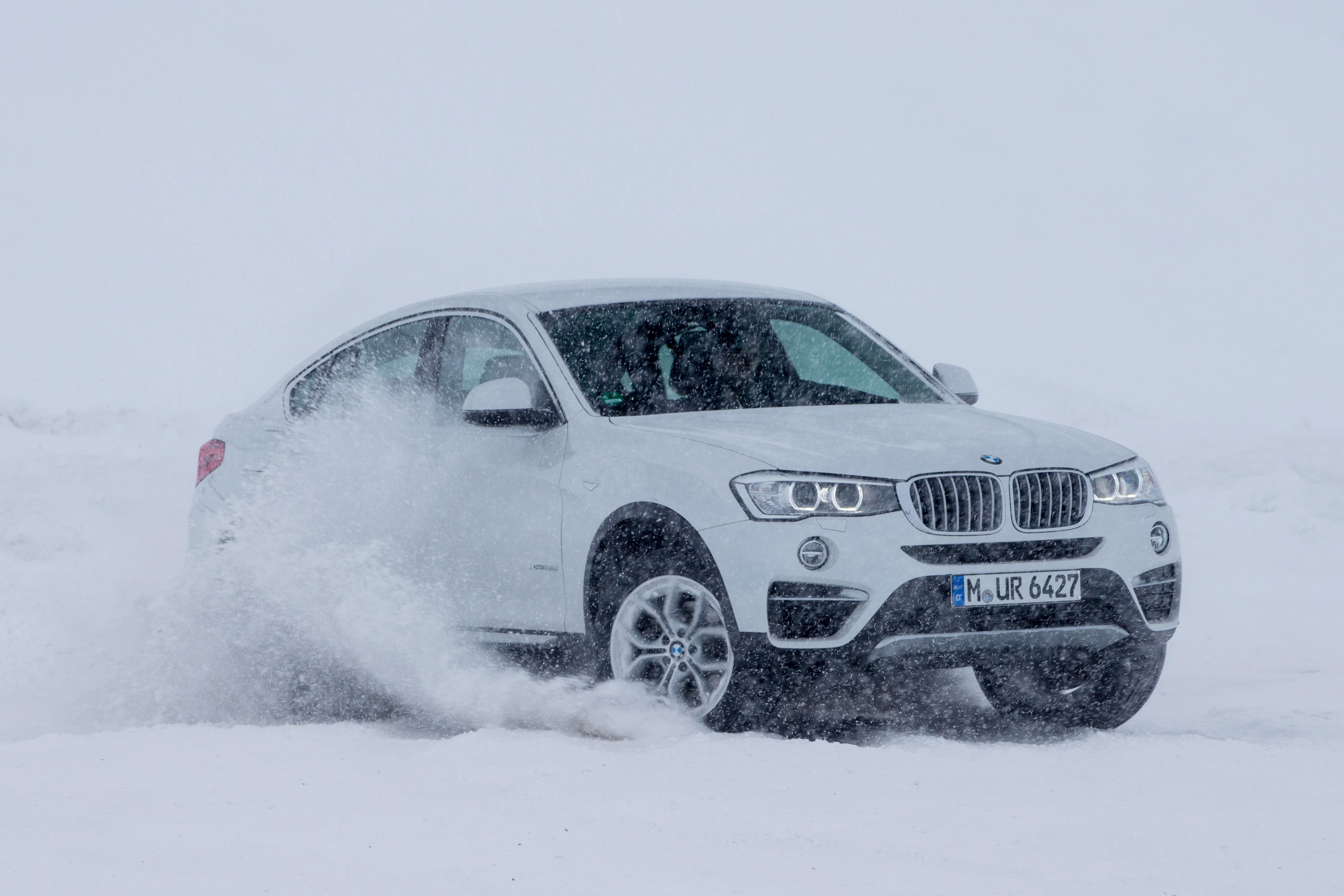 Weißer SUV fährt durch dichten Schnee und spritzt ihn auf, während er auf verschneiter Fläche unterwegs ist.