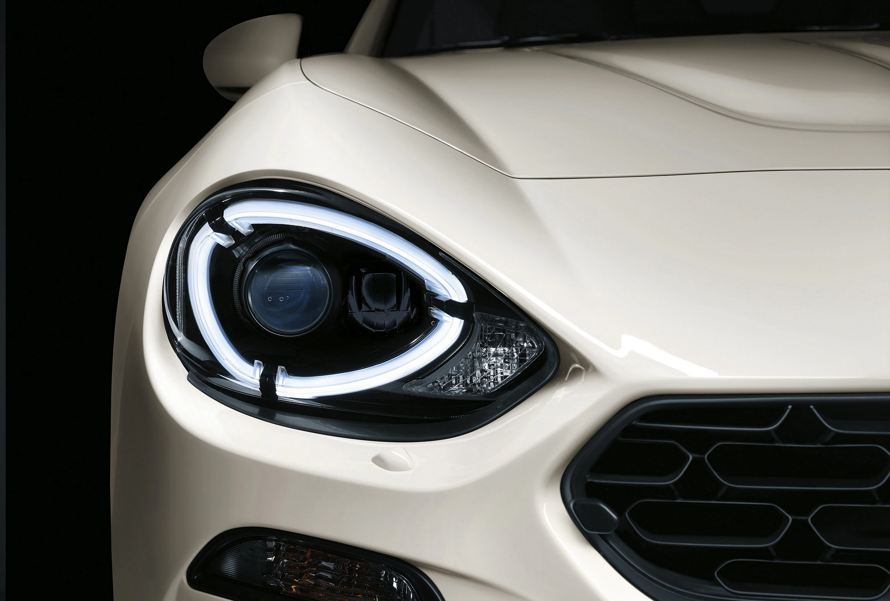 Beiger Sportwagen im Profil, zeigt markante Frontscheinwerfer und Kühlergrill gegen schwarzen Hintergrund im Detail.