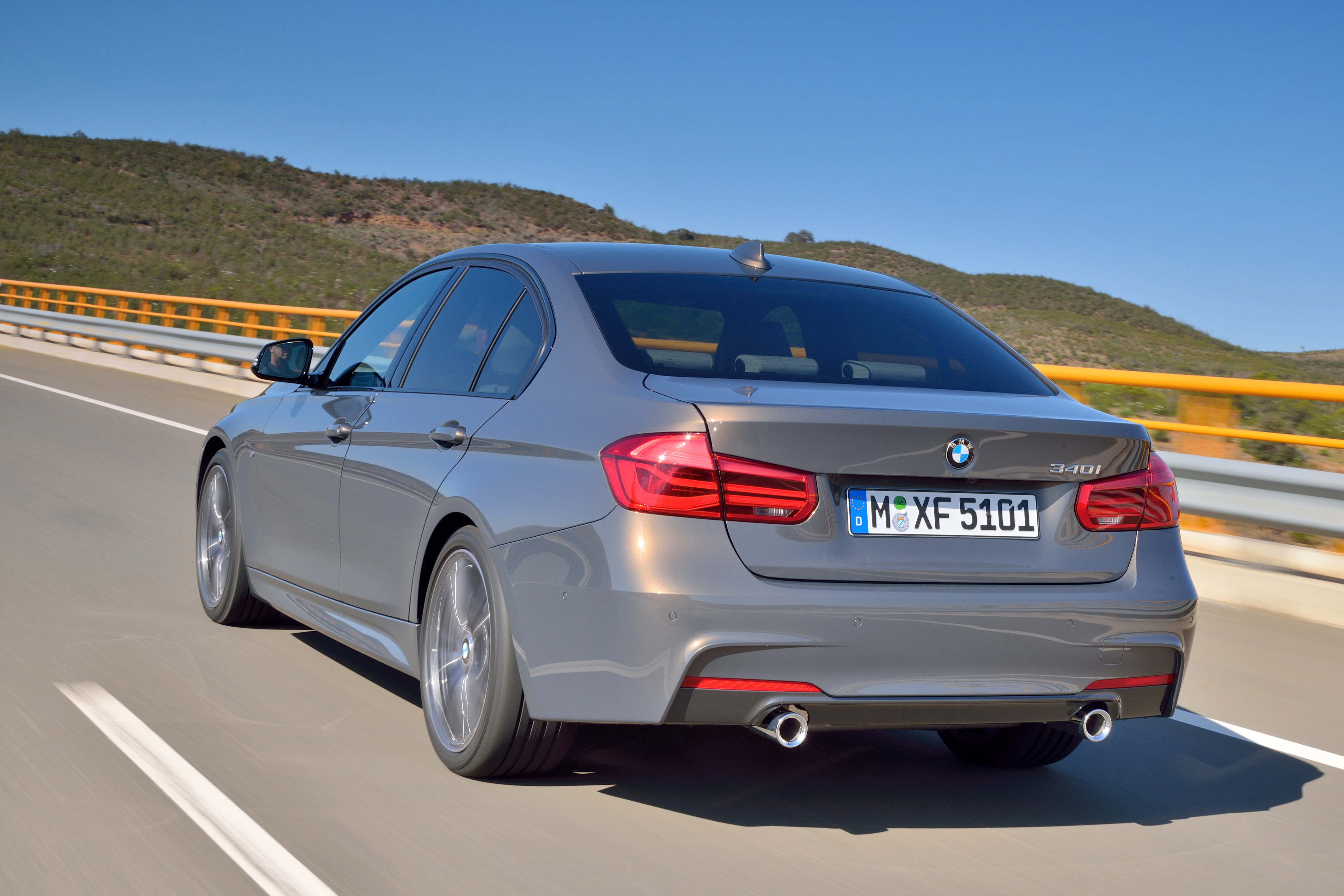 Silberner BMW 3er fährt auf einer Autobahn bei Sonnenschein. Im Hintergrund sind hügelige Landschaften zu sehen.