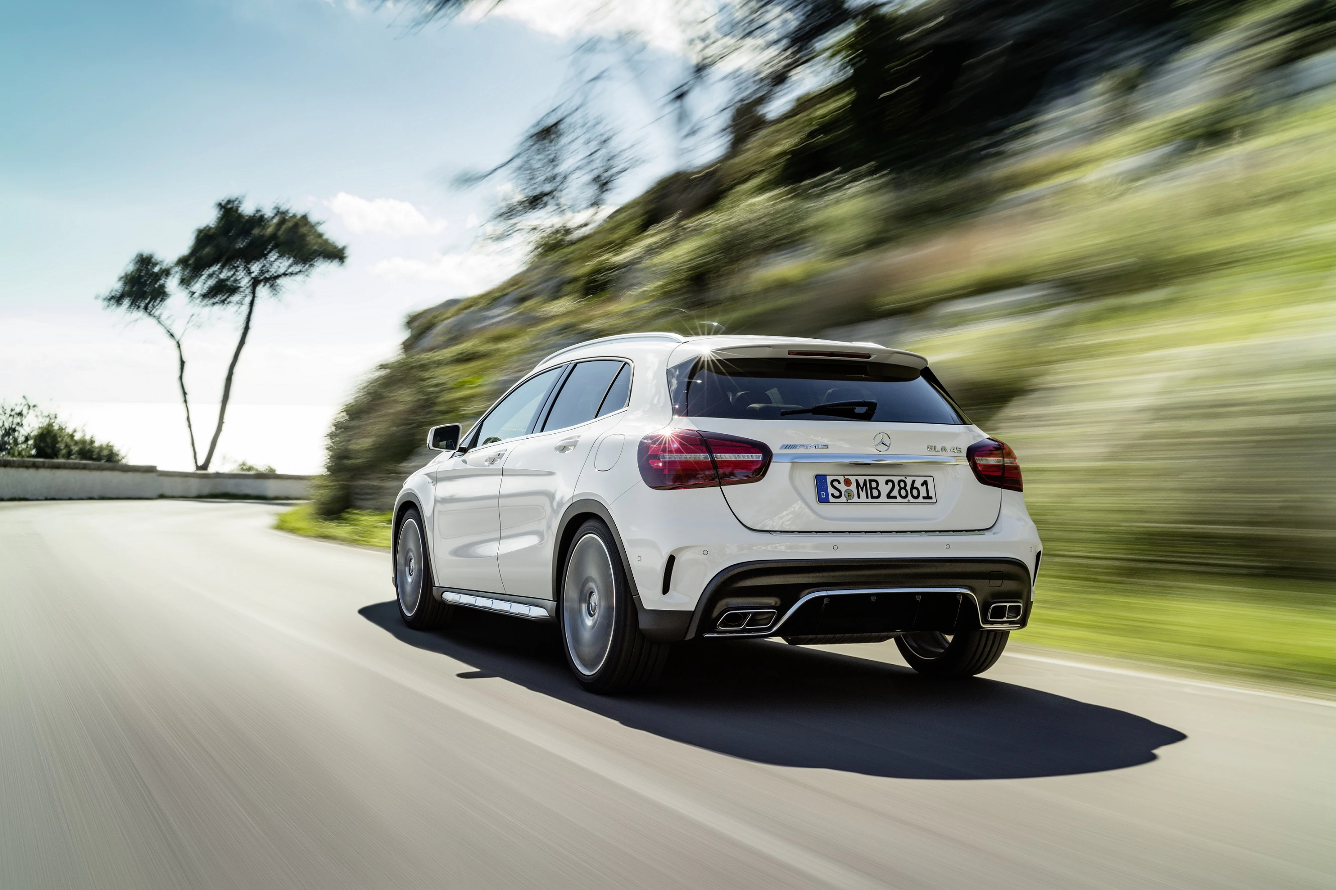 Weiße Limousine fährt dynamisch eine kurvenreiche Straße entlang, Bäume und Himmel im Hintergrund, mit Bewegungsunschärfe.