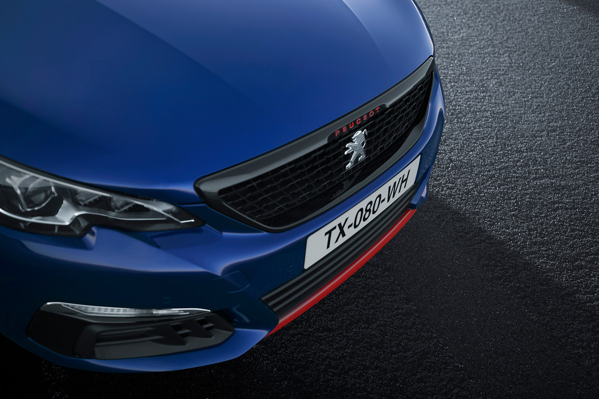 Nahaufnahme eines blauen Peugeot mit sichtbar rotem Detail an der Frontstoßstange, auf nassem Asphalt geparkt.