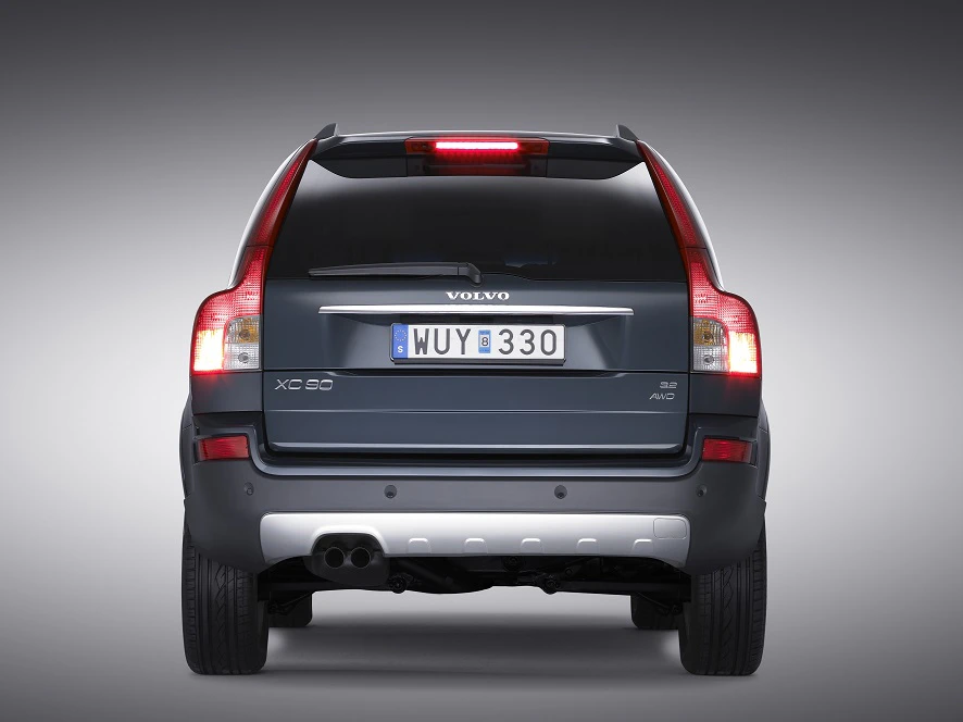 Rückansicht eines grauen Volvo XC90 SUV, beleuchtete Rücklichter, Nummernschild "MUY 330", vor grauem Hintergrund.