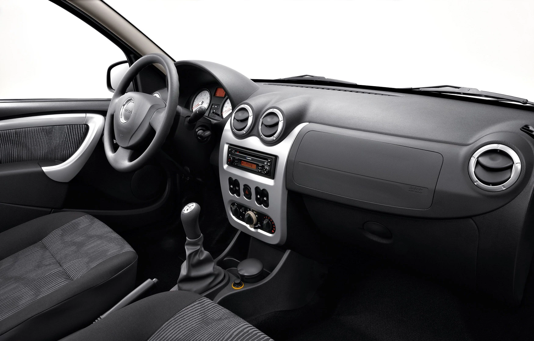 Innenraum eines Autos mit schwarzer Polsterung, Lenkrad links, und Armaturenbrett mit Radio und Lüftungsschlitzen.